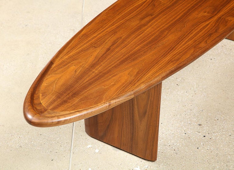 Walnut. Elliptical table top with bull-nose edge and 2 wedge-shaped supports. Signed with makers decal on underside of top.