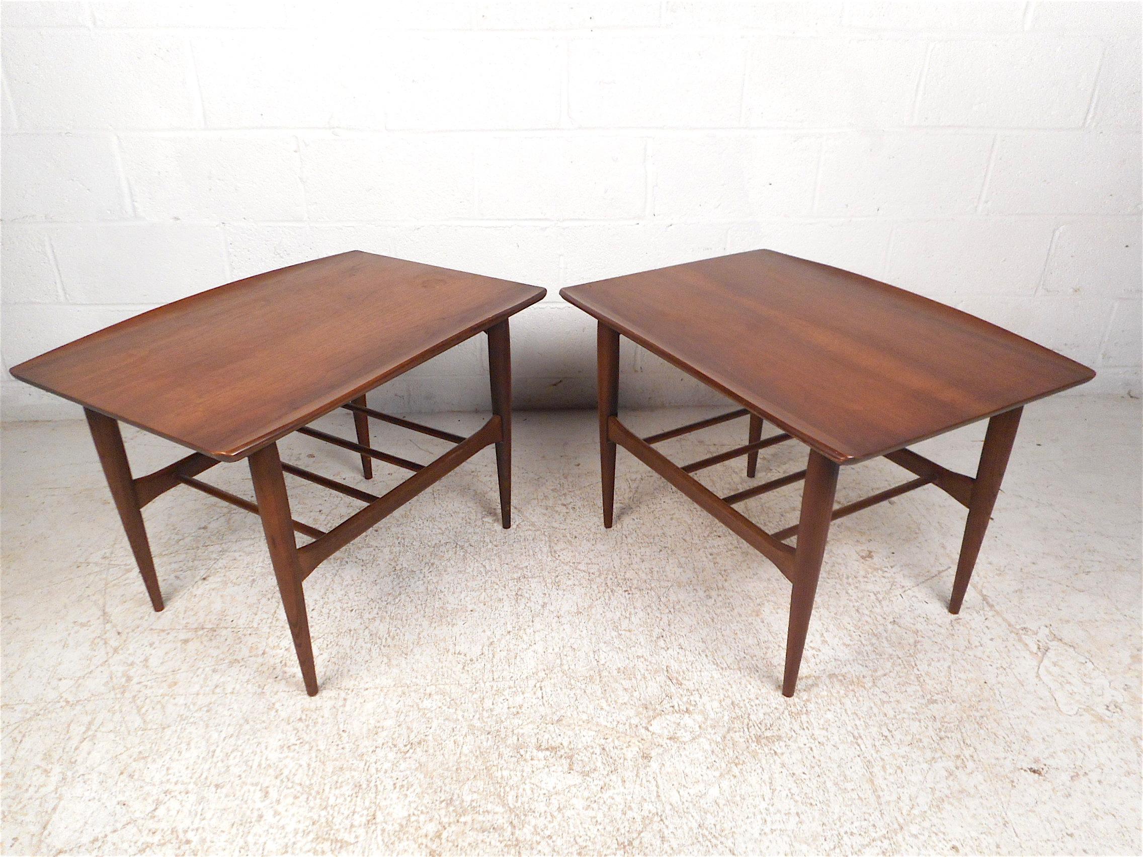 Stylish pair of midcentury end tables by Bassett Furniture Company, circa 1960s. Sturdy walnut construction. Raised edges on the tabletops combined with tapered legs give these tables a striking visual profile. Sure to be a great addition to any