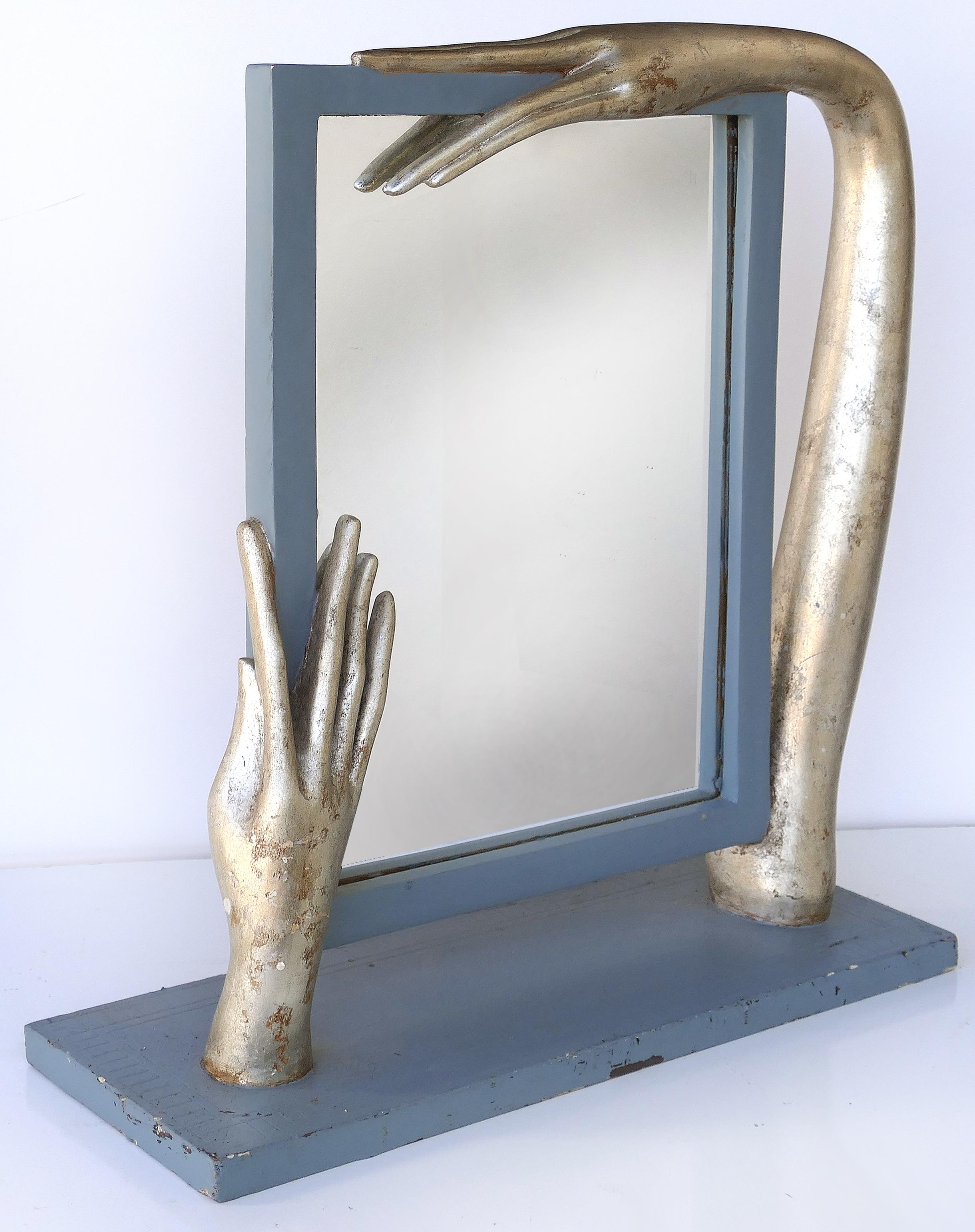 Surrealist carved wood table standing mirror

Offered for sale is a Surrealist carved wood table mirror with silver leaf hand details. This sculptural mirror shows movement through the exaggerated stylized carved hands. This is juxtaposed to a