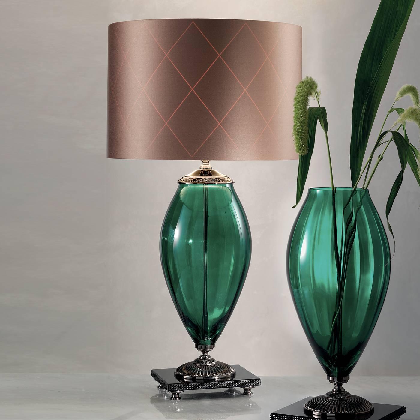 A glamorous accent perfect for any space, this eye-catching lamp showcases a green glass body with a gold-plated decorative accent around the top. Resting atop a black square marble base accented with black rhinestones, the lamp sits on an ornate