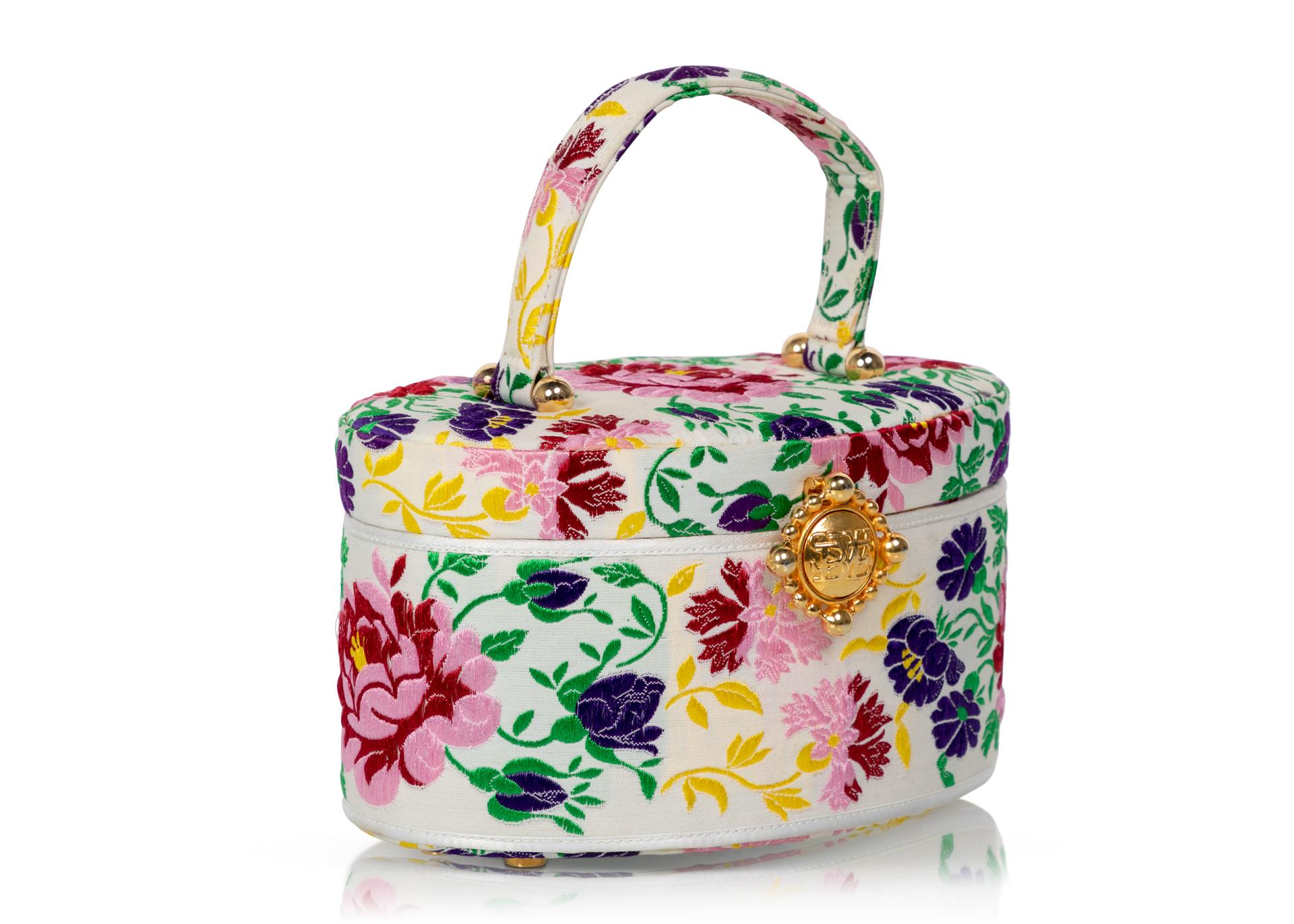 Susan Bennis Warren Edwards vintage top handle bag done in Ivory and multicolor woven silk floral brocade done in purple, pink, red and yellow with green leaves. The bottom of the bag has six gold feet each set with a pearl. The bag is lined in