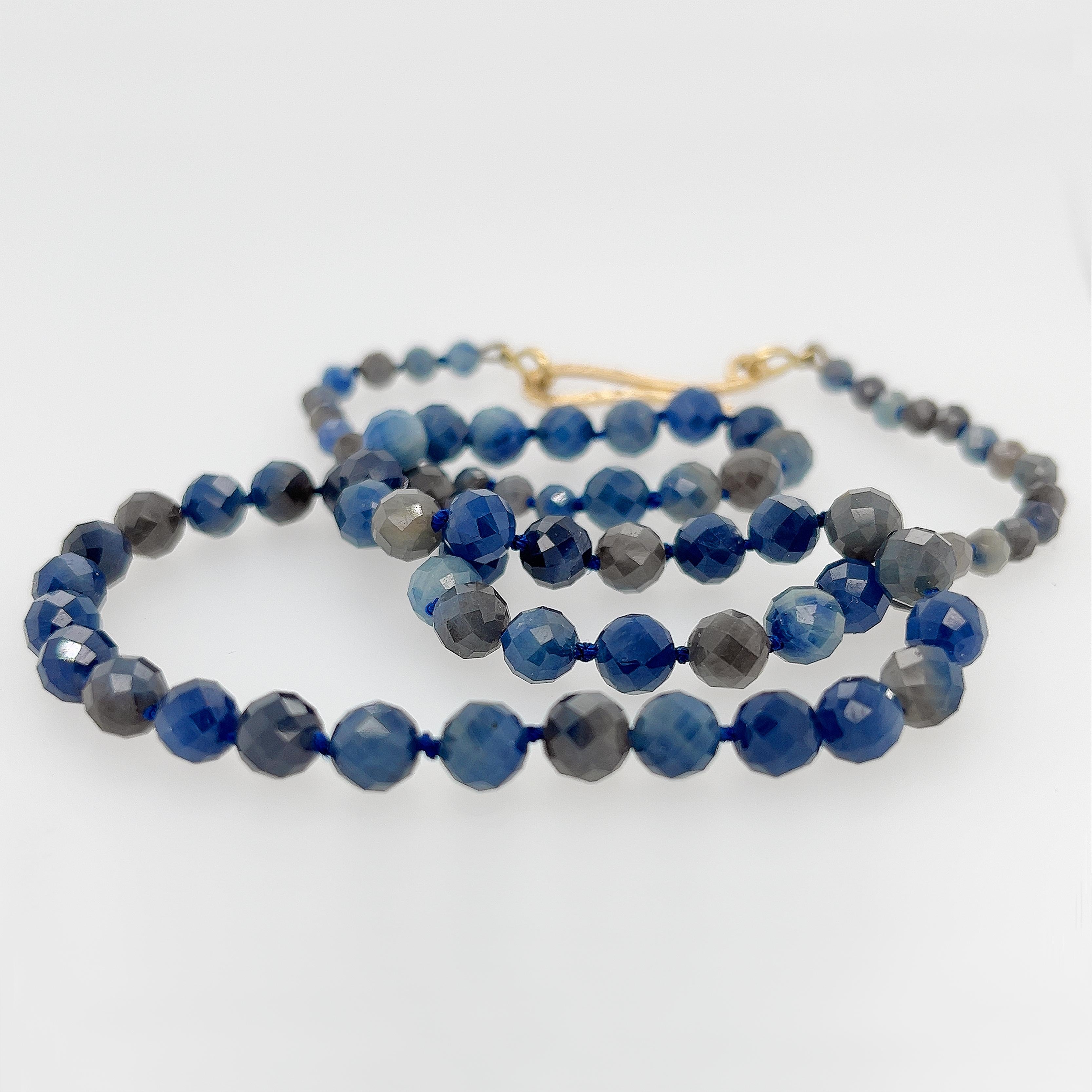 Every time you turn while wearing this one-of-a-kind Faceted Sapphire, Silk and 18kt Yellow Gold Necklace, the sapphires sparkle brightly.
The untreated and undyed sapphire beads are all different shades and hews of luscious blues into blue-grays