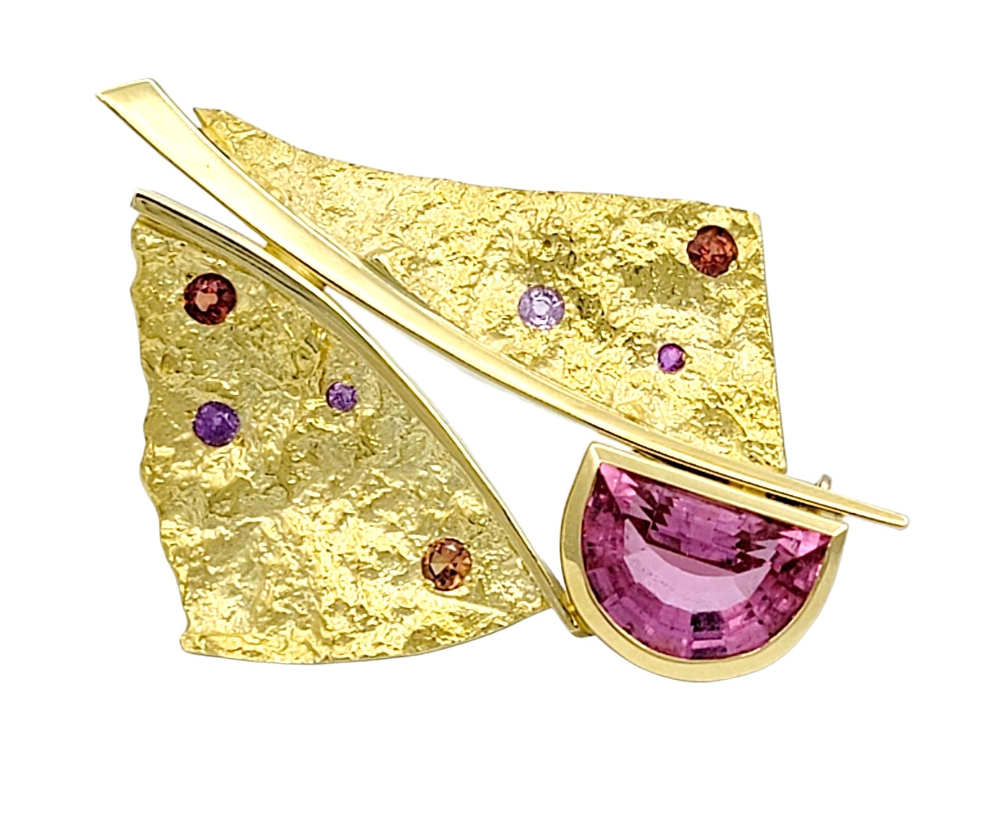 This Susan Helmich brooch is a magnificent creation that seamlessly combines bold design and vibrant gemstones. Set in lustrous 18-karat yellow gold, the brooch features a large half-moon-shaped pink tourmaline as the main focal point, radiating