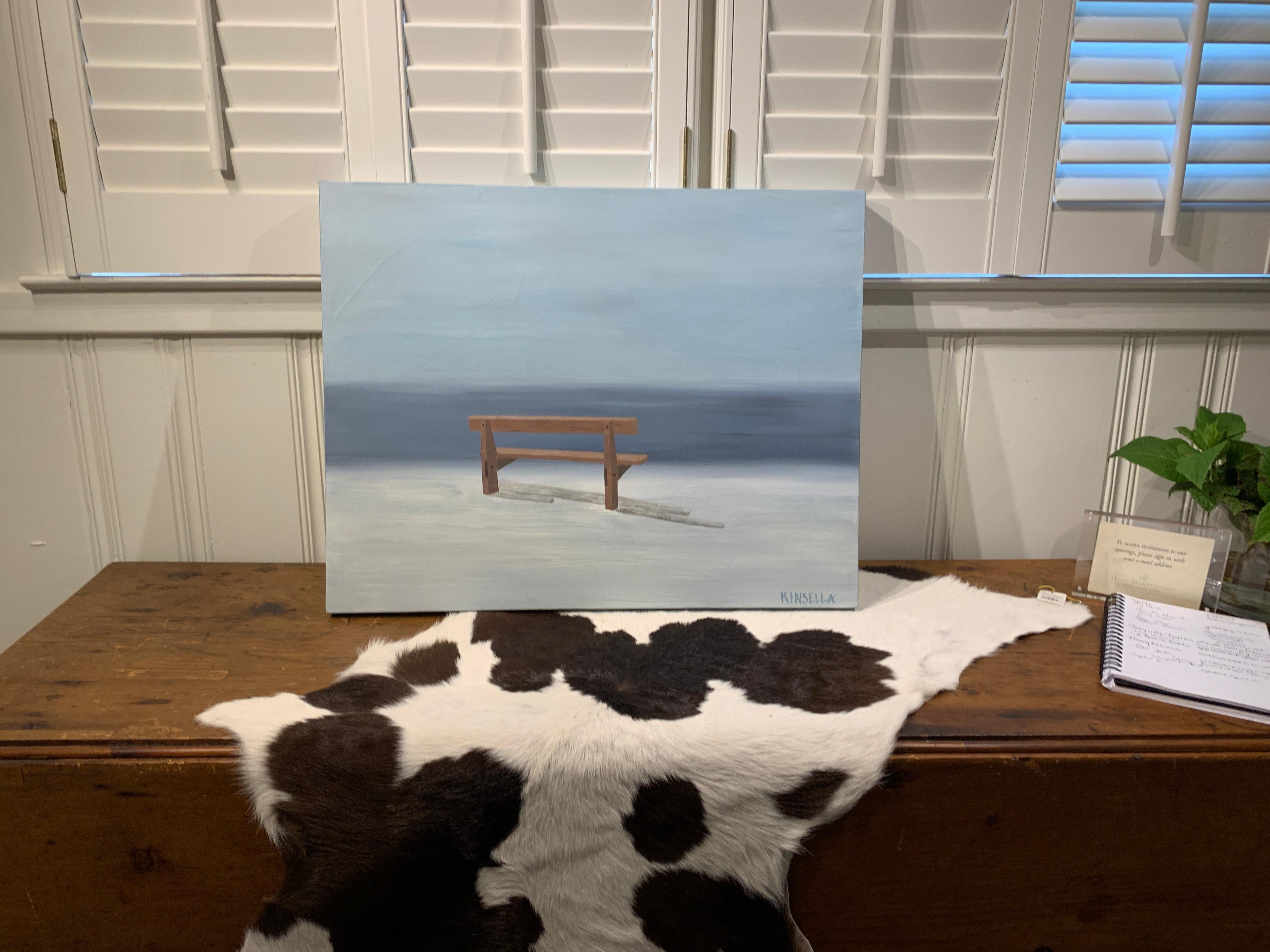 'Still Resting' is a small contemporary acrylic on canvas painting created by American artist Susan Kinsella in 2019. Featuring a palette made of grey and brown tones, the painting depicts a humble bench overlooking the sea. We are immediately