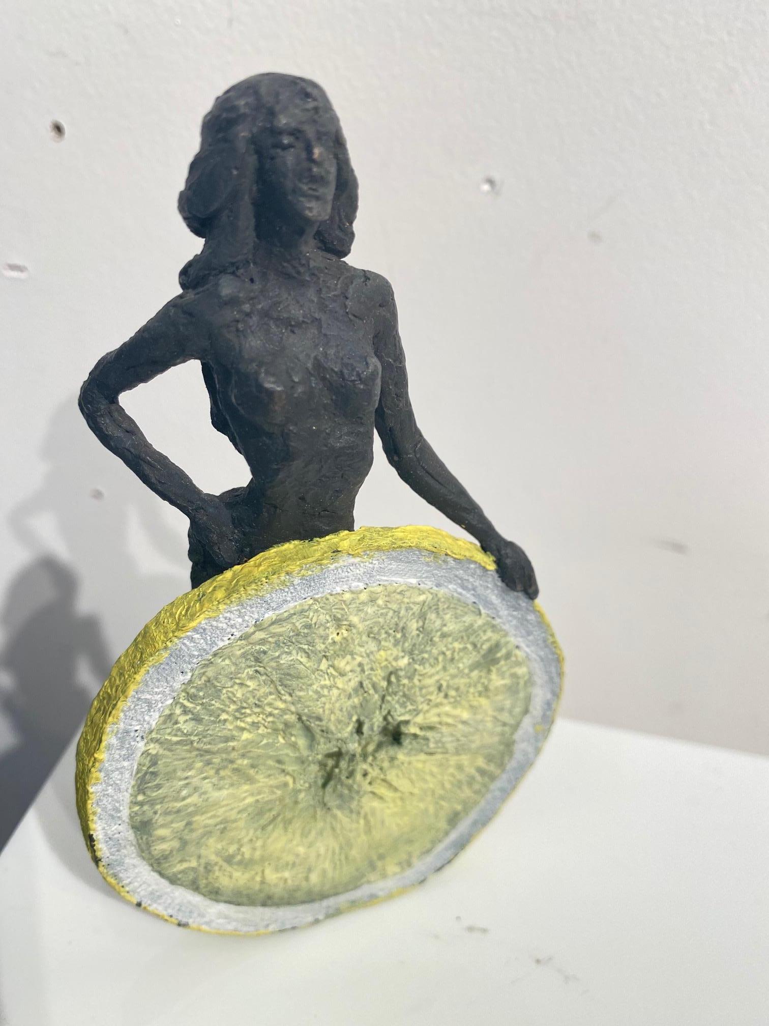 "The Beautiful Sparkle" is a small free-standing bronze sculpture of a standing nude female behind a yellow lemon. Edition 18, signed, numbered and dated on the bottom. 

The sculptress Susanne Kraisser is to be considered as part of the great