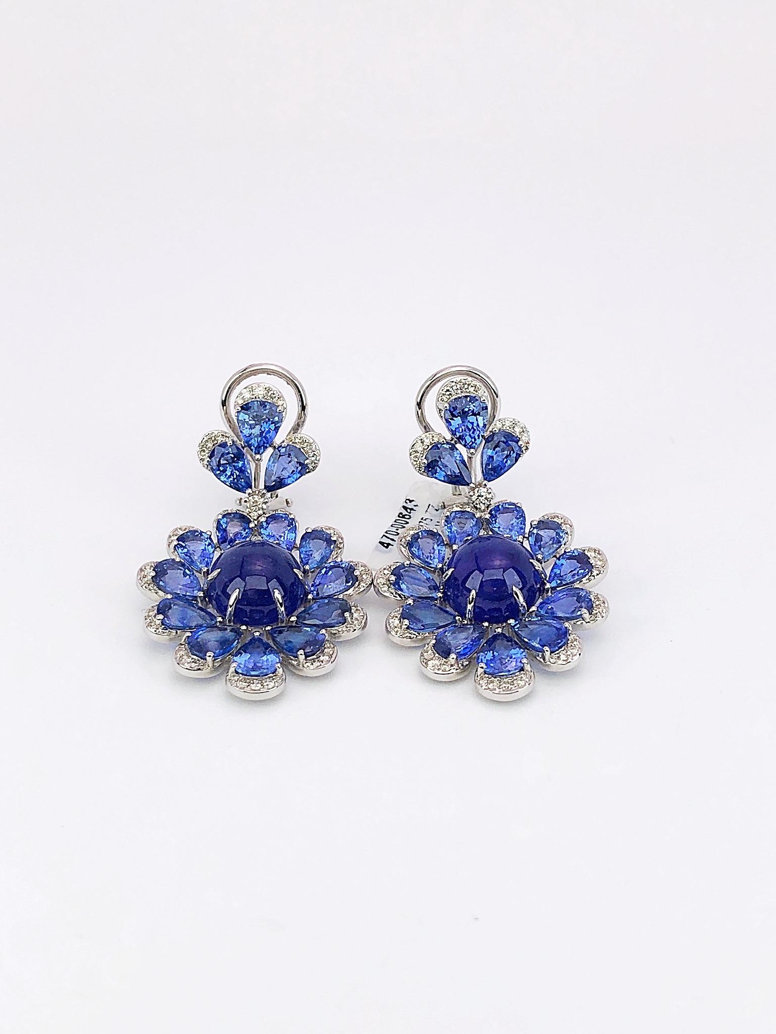 These stunning earrings are  composed of round cabochon tanzanite centers that are surrounded by pear shaped blue sapphires, and accented with round brilliant diamonds. Set in 18-karat white gold.
The earrings are 1.75