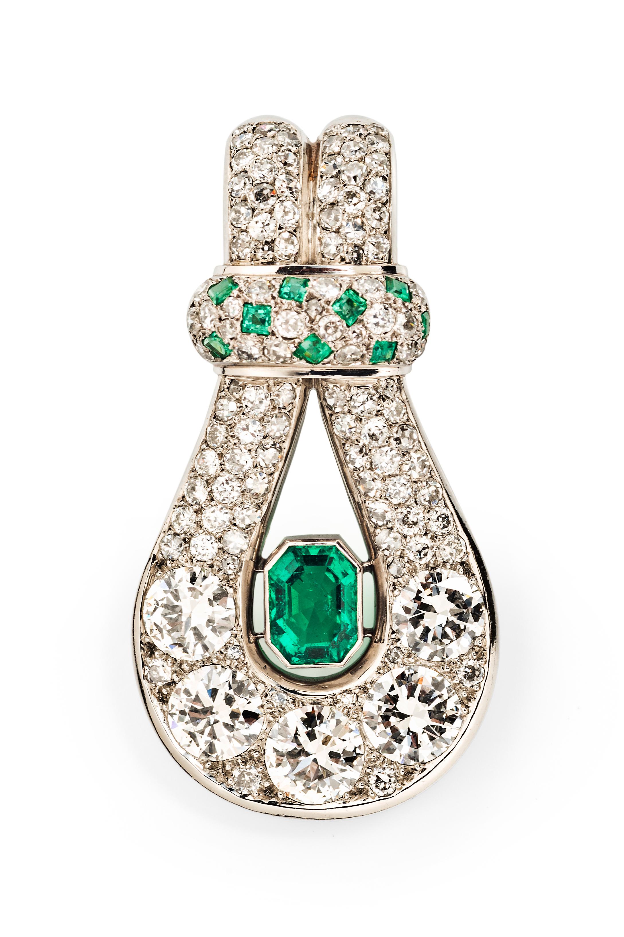 This extraordinary mid-century jewel by Suzanne Belperron consists of a lyre-shaped emerald and diamond detachable pendant brooch suspended from two rows of cultured pearls interspersed with green glass beads and finished with a platinum clasp set