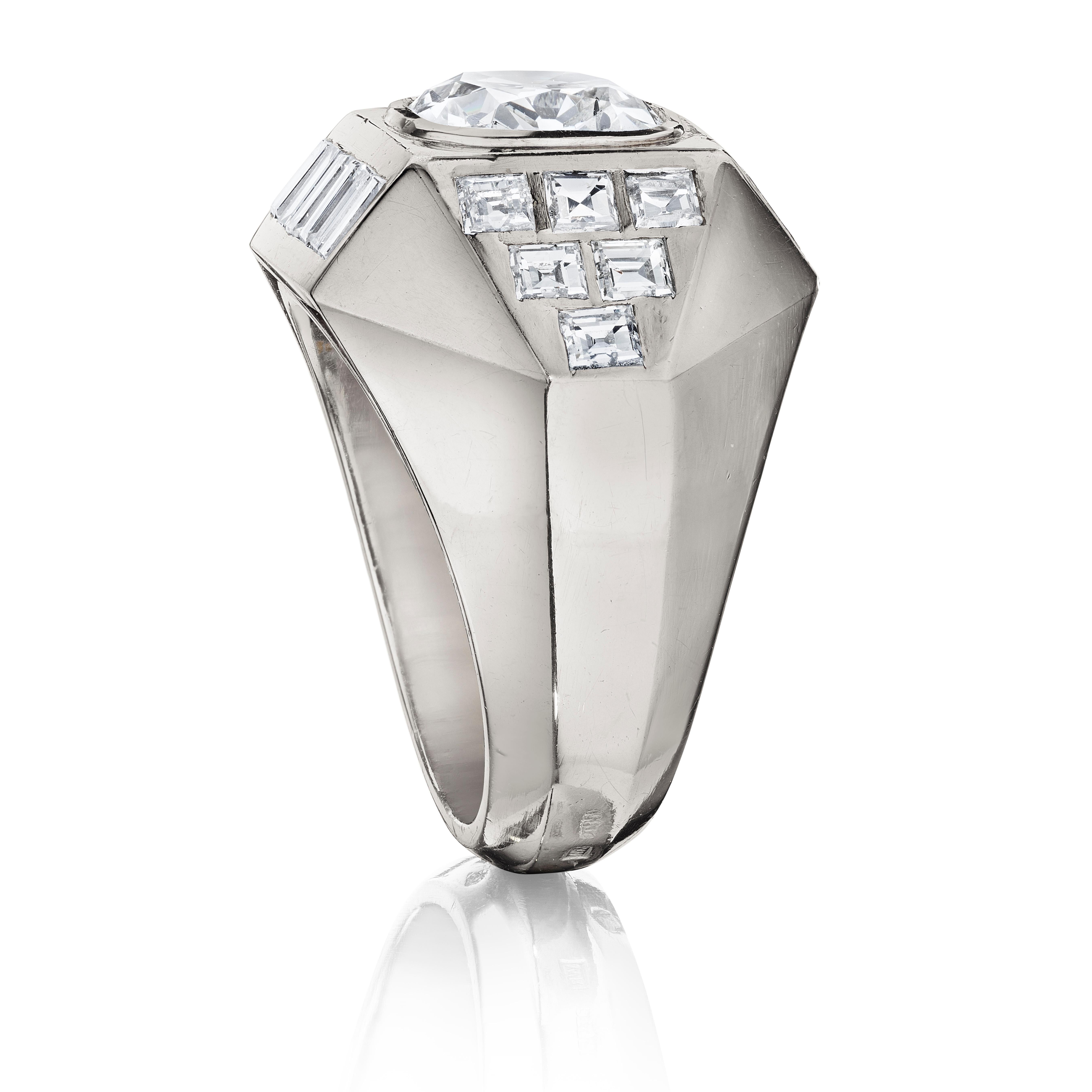 A ring designed with a central bezel-set cushion diamond sided by intersecting platinum planes set with square and rectangular diamonds; mounted in platinum, with French assay marks
• 1 cushion-cut diamond, weighing approximately 2.95 carats
• 12