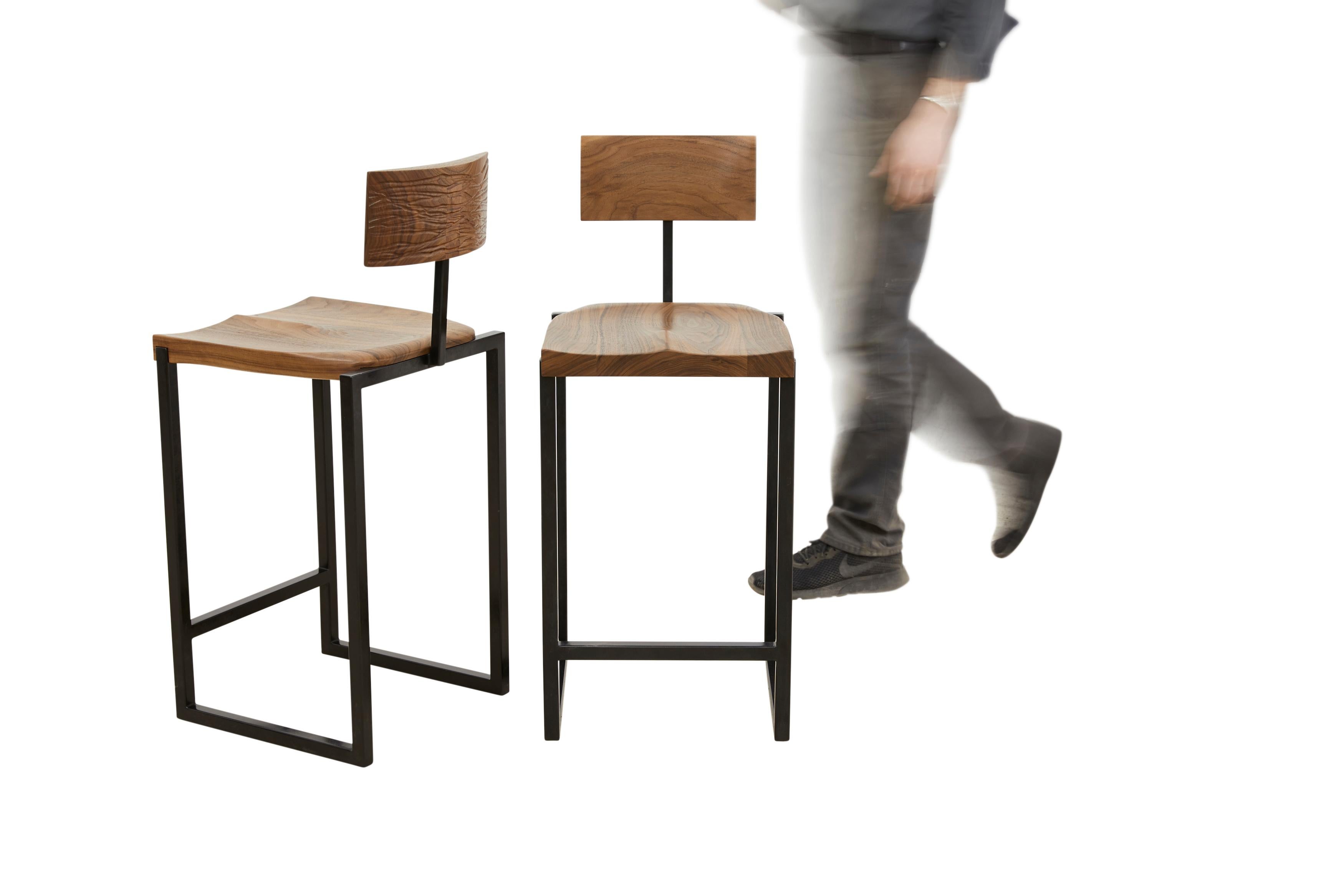 This stool is composed of a hand-shaped walnut wood seat and backrest that sits upon a blackened steel frame. Finished with oil, the rear face of each backrest features a unique carved drawing.