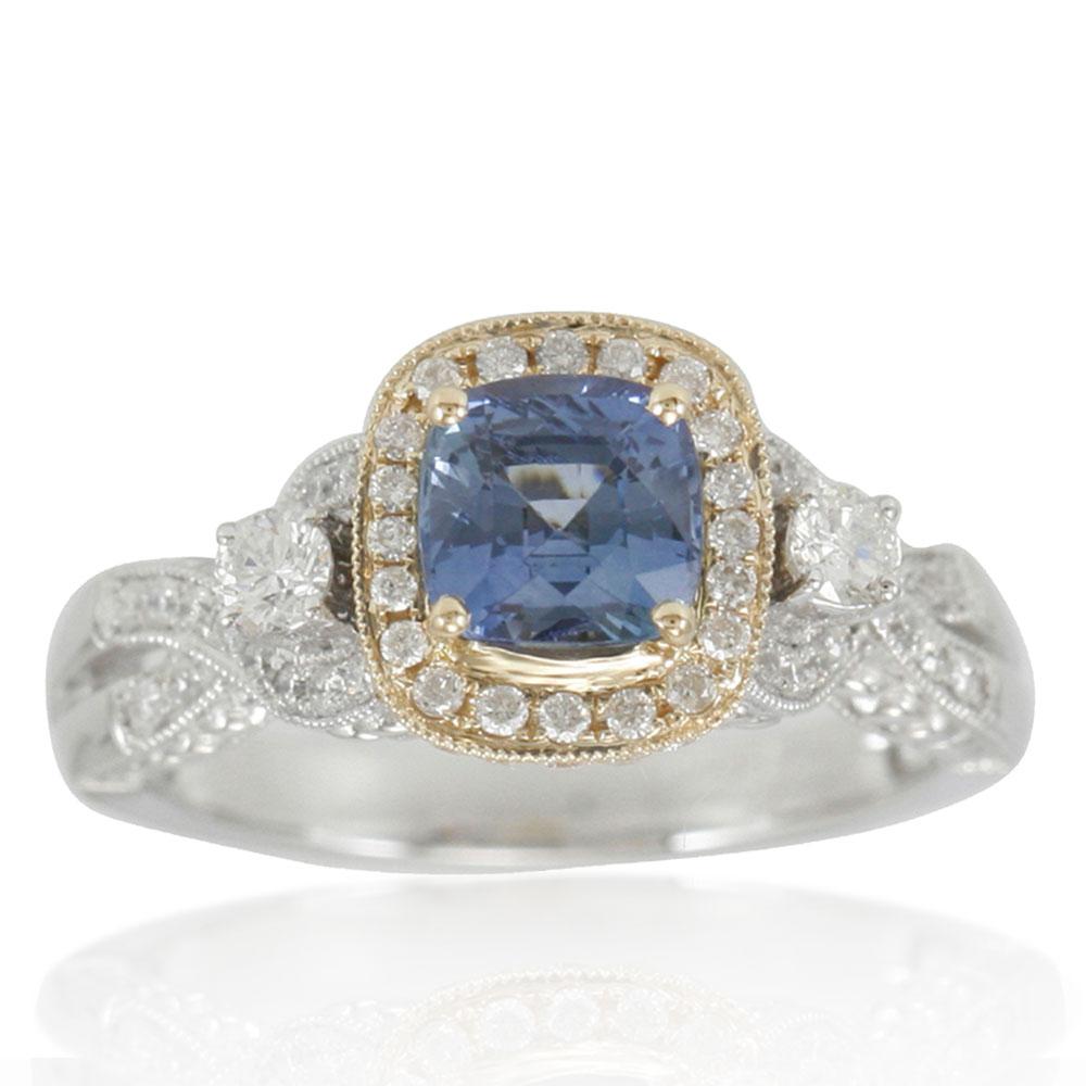 This spectacular ring from the Suzy Levian Limited Edition collection features a blue sapphire gemstone held in a 14K gold two-tone white and yellow prong setting. An array of side white diamonds (.76ct) with hand-carved French filigree work across