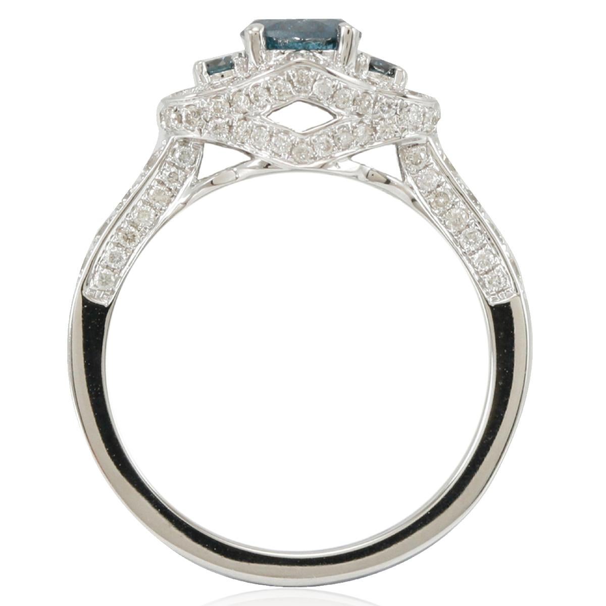 This strikingly gorgeous, one-of-a-kind engagement ring by Suzy Levian is a 3-stone blue diamond solitaire with a white diamond pave halo. Elegantly crafted in 14K white gold, this ring features a brilliant-cut round blue diamond center stone