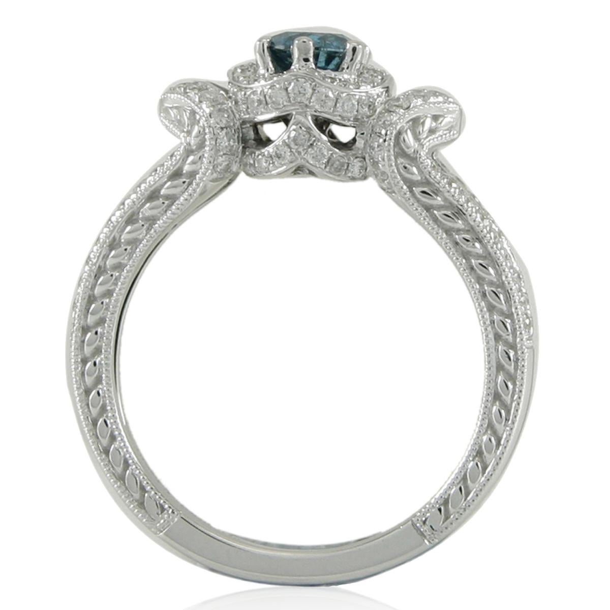 This strikingly gorgeous engagement ring by Suzy Levian is elegantly crafted in 14K white gold featuring a brilliant-cut round blue diamond center stone (0.42ct). This diamond ring features artistic pave diamond artwork all across the band, as it