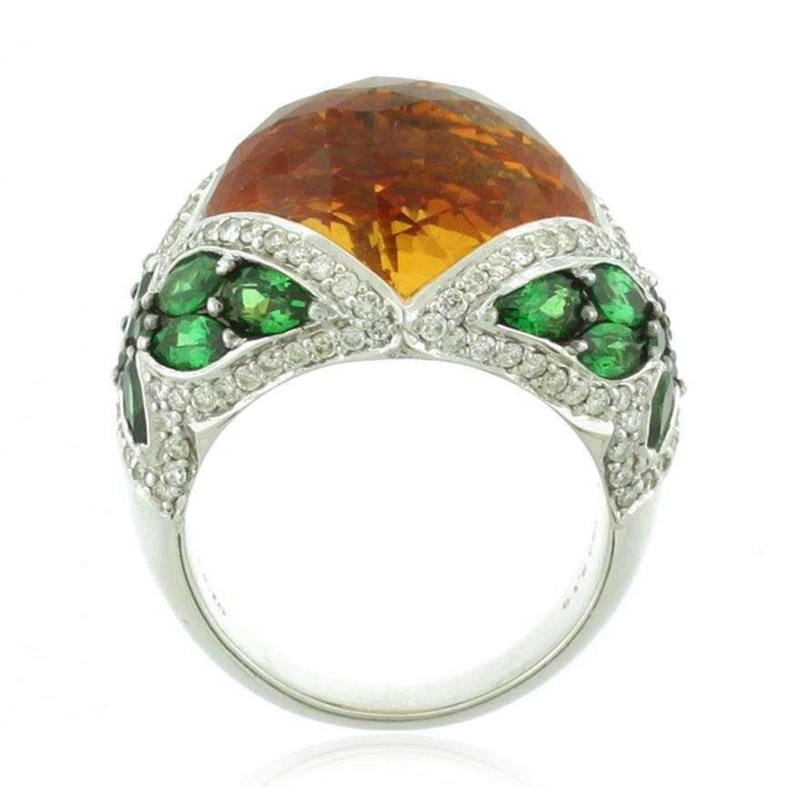 This elegant designer ring features a large checkered oval cabochon citrine center stone weighing 12.70ct, surrounded by 120 white pave diamonds totaling 1.20ct TDW. The sides of the ring are different cuts of green tsavorite stones coming together