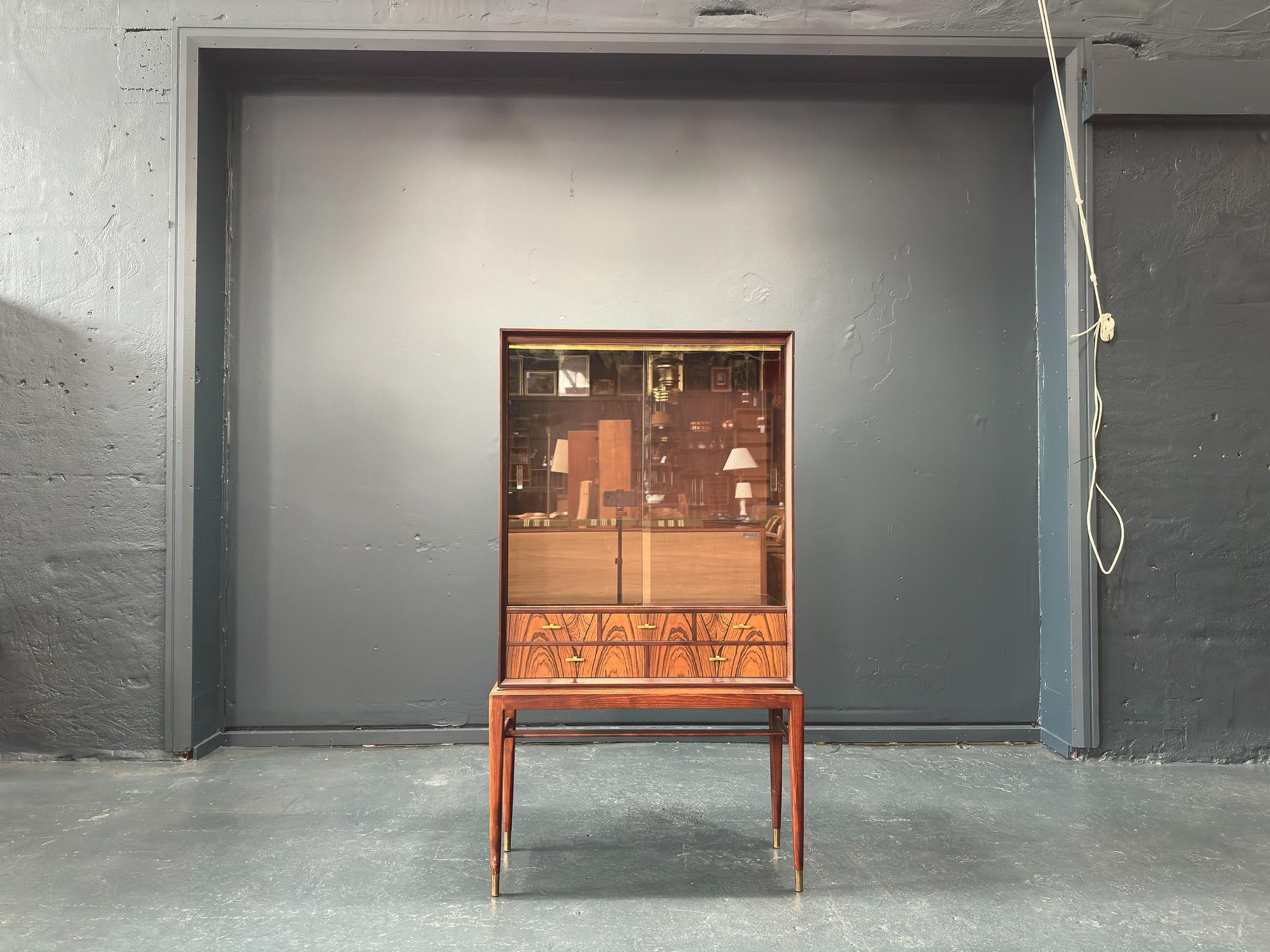 This 1960s cabinet, titled the 'Cortina'  is Swedish in origin and was designed by Svante Skogh for Säffle Möbelfabrik.

It is set on a very elegant slimline hardwood frame, with tapered legs finished with brass feet that match the decorative curved