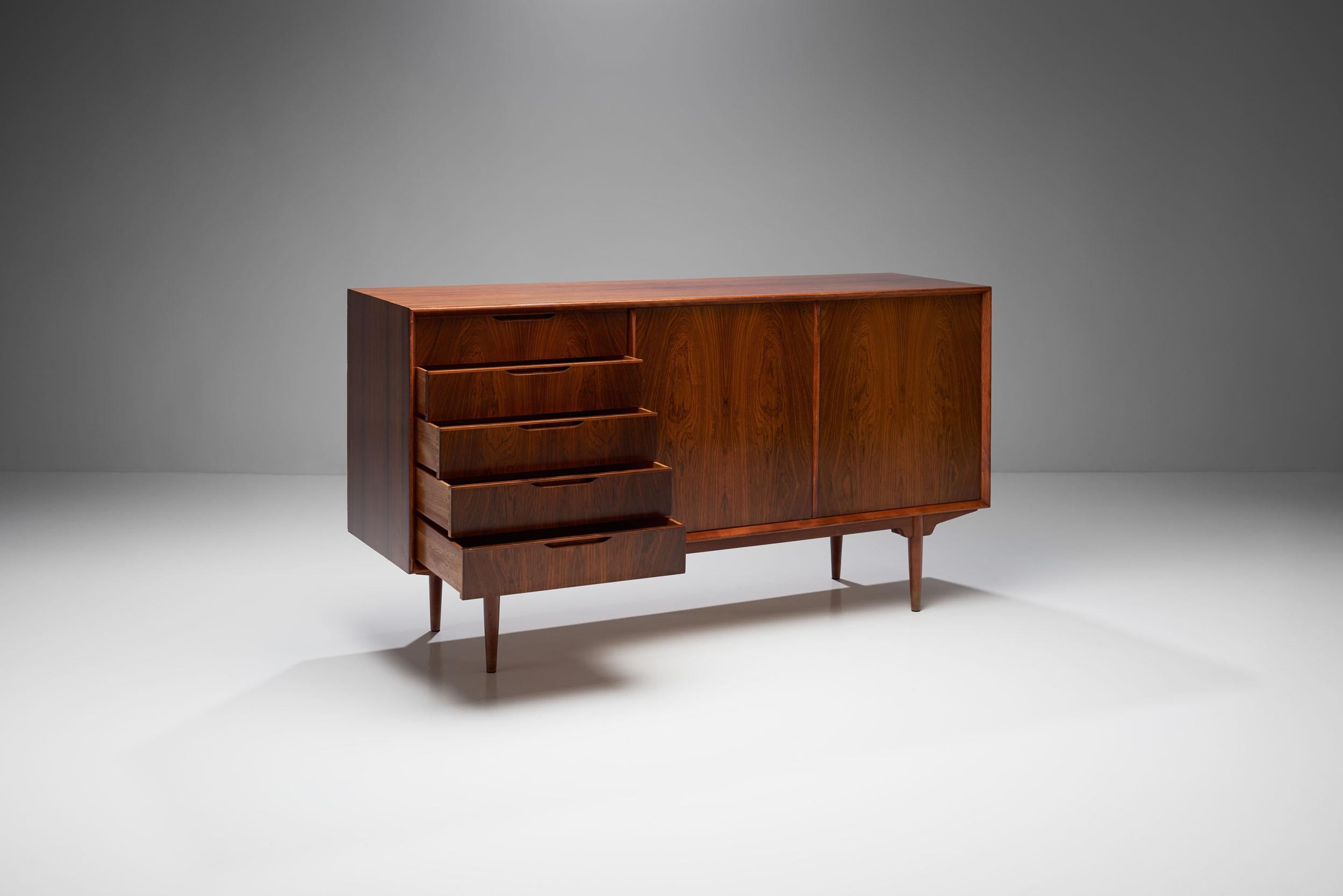 A Svante Skogh “Silvia” sideboard with two sliding doors and five drawers, produced by AB Seffle Möbelfabrik. 

This sideboard features a practical design with its sliding doors and drawers, paired with wooden material. It features sleek and