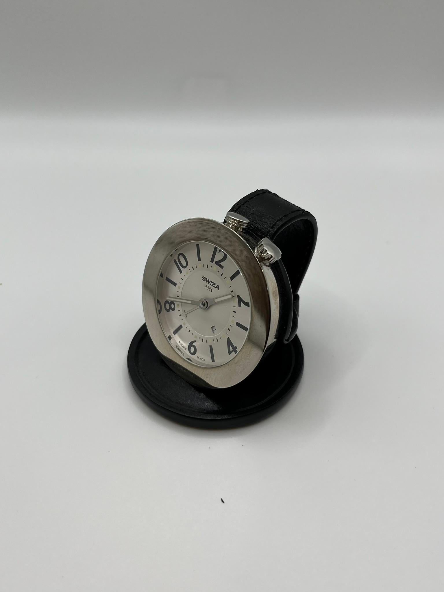 Elegant Swiza travel alarm clock, made of steel with black leather folding custiodia. It was made in Switzerland and mounts a quartz movement. It provides excellent legibility thanks to a white dial with black Arabic numerals and a date window. It