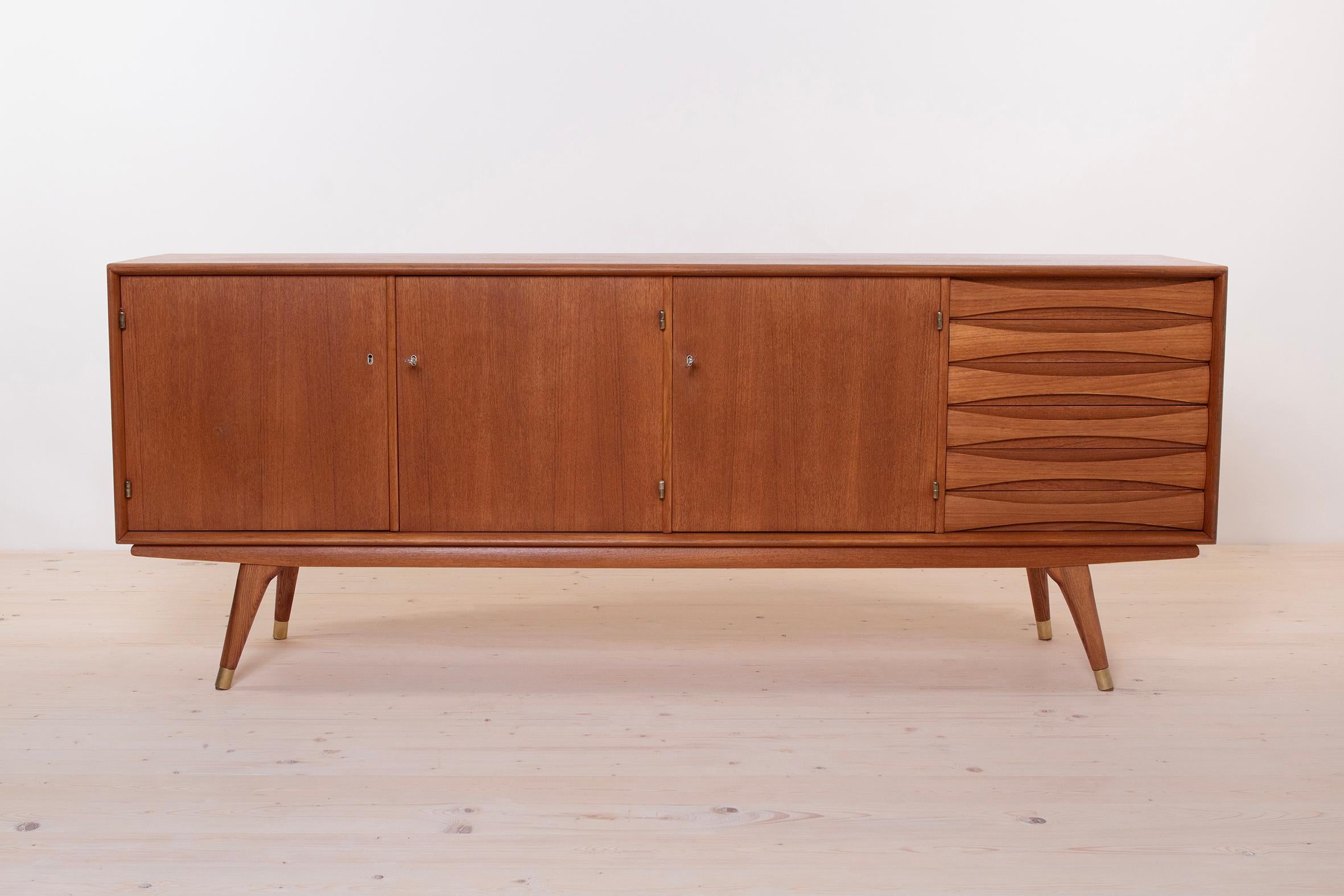 This beautiful teak sideboard was designed by Sven Andersen and manufactured in Norway in second half of the 1950s. The piece features three doors that reveal lots of storage space and six drawers in the section on the right. The sideboard features