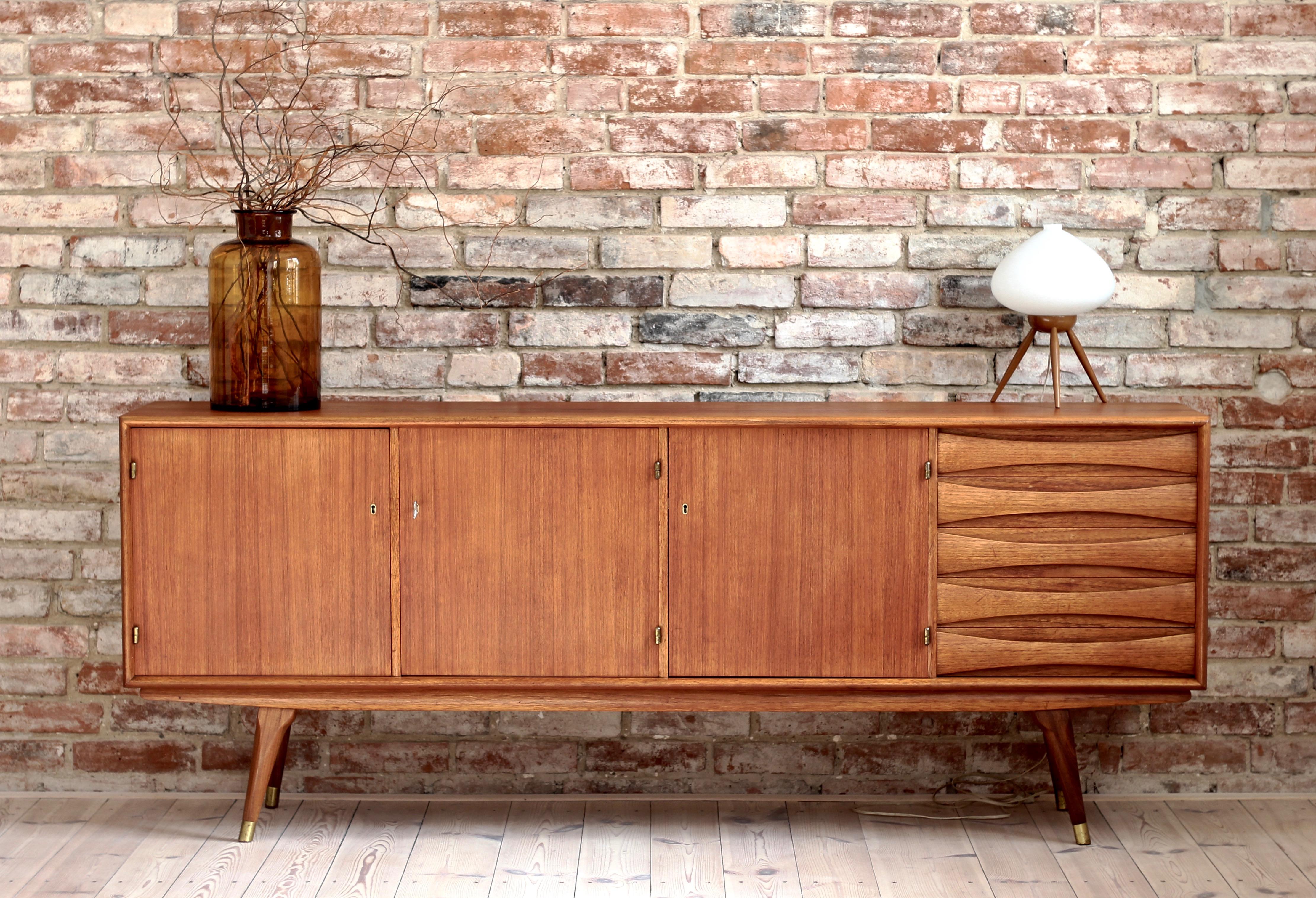 This is a quite rare Sven Andersen teak sideboard designed and manufactured in Norway around second half of 1950s. The piece features three doors that reveal lots of storage space and five drawers in the section on the right. The sideboard features