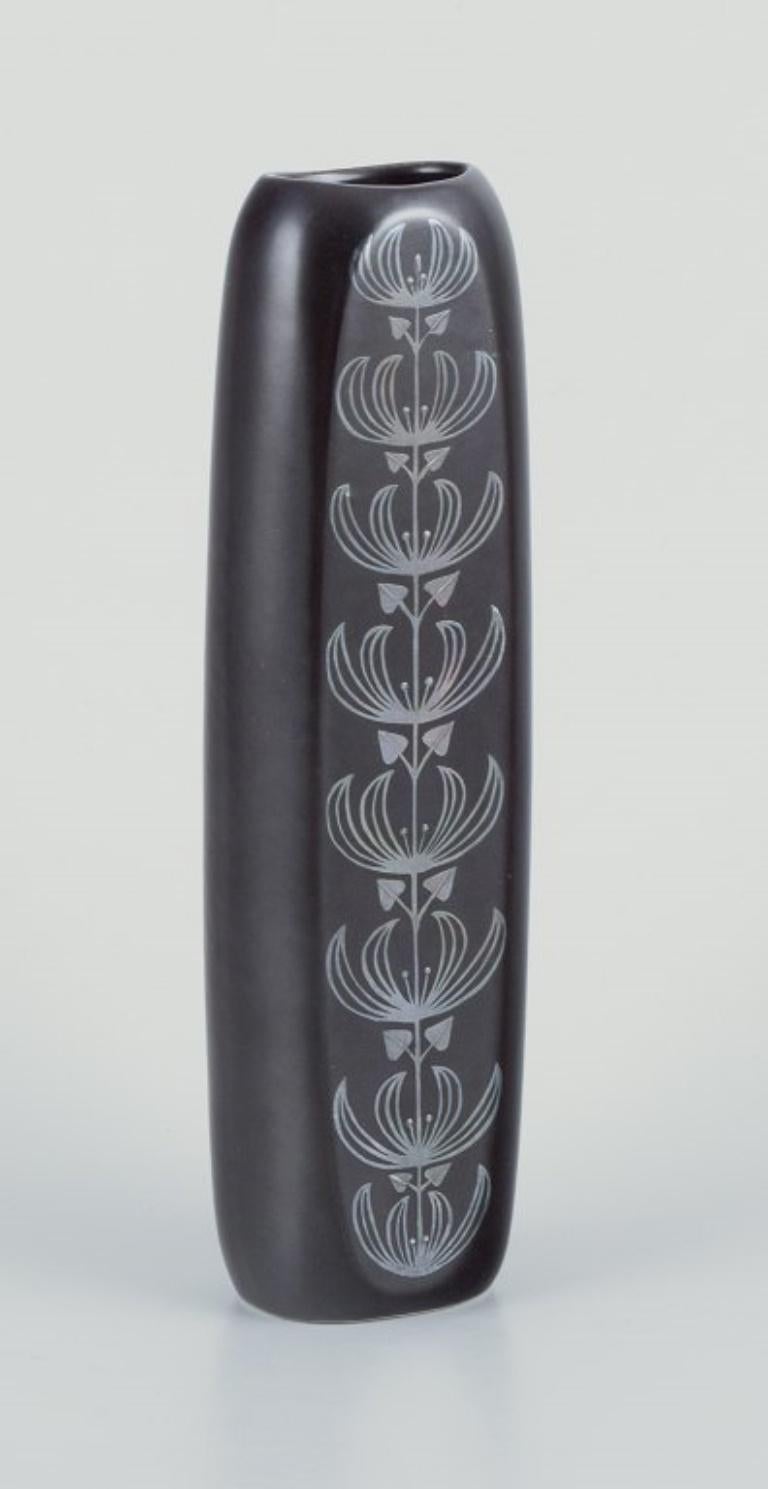 Sven Johnson for Gustavsberg. 
“Facett” ceramic vase.
Motif of peacock and flowers in silver decoration.
Brown glaze.
1970s/80s.
Marked.
Perfect condition.
Dimensions: Height 25.0 cm. x Width 7.0 cm. x Diameter 5.0 cm.