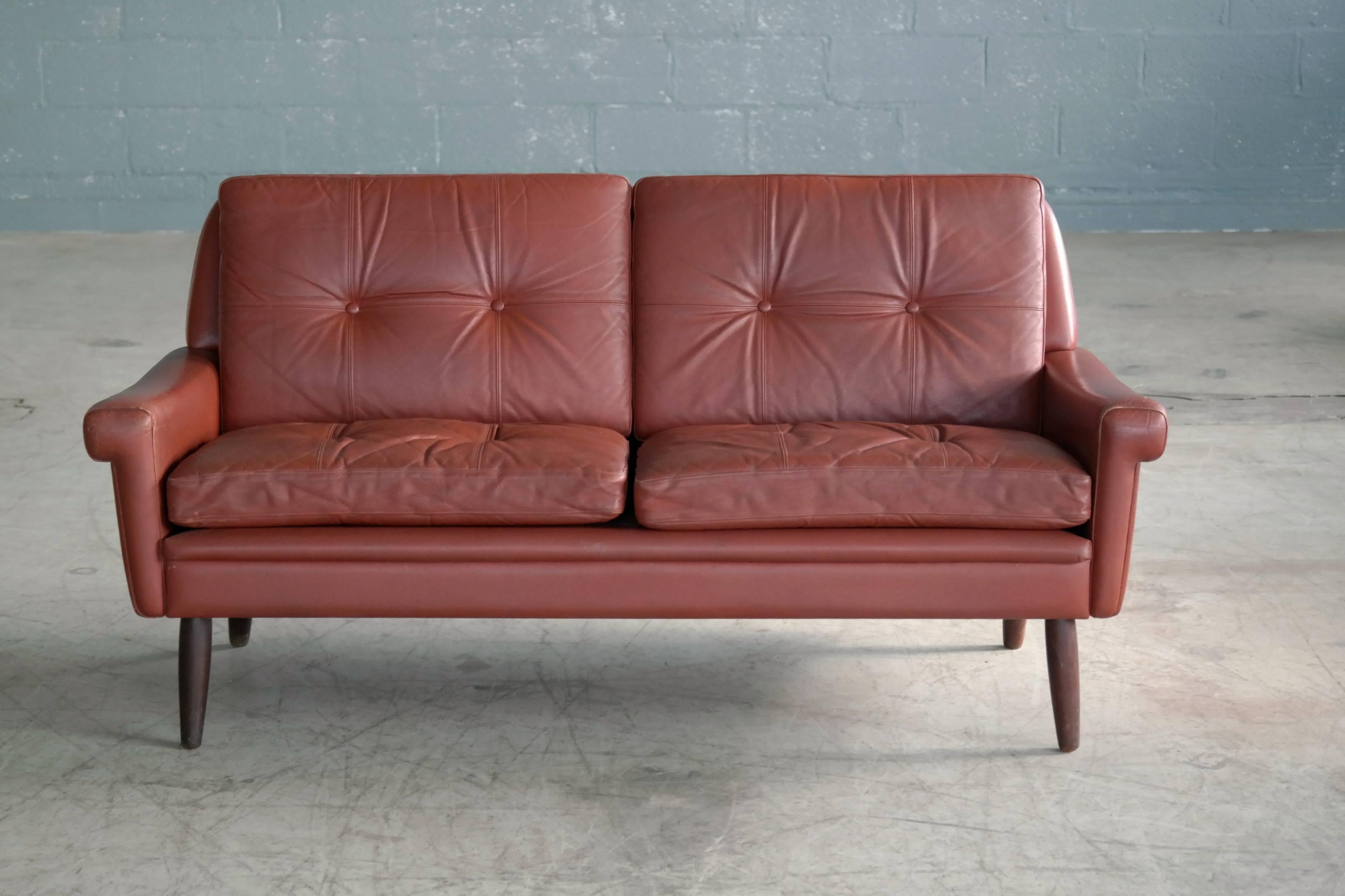 Wonderful loveseat or two-seat sofa designed by Sven Skipper in the 1960s. With loose cushions upholstered in buttoned reddish brown colored leather raised on stained beech legs. Overall very good condition with some natural age wear and patina