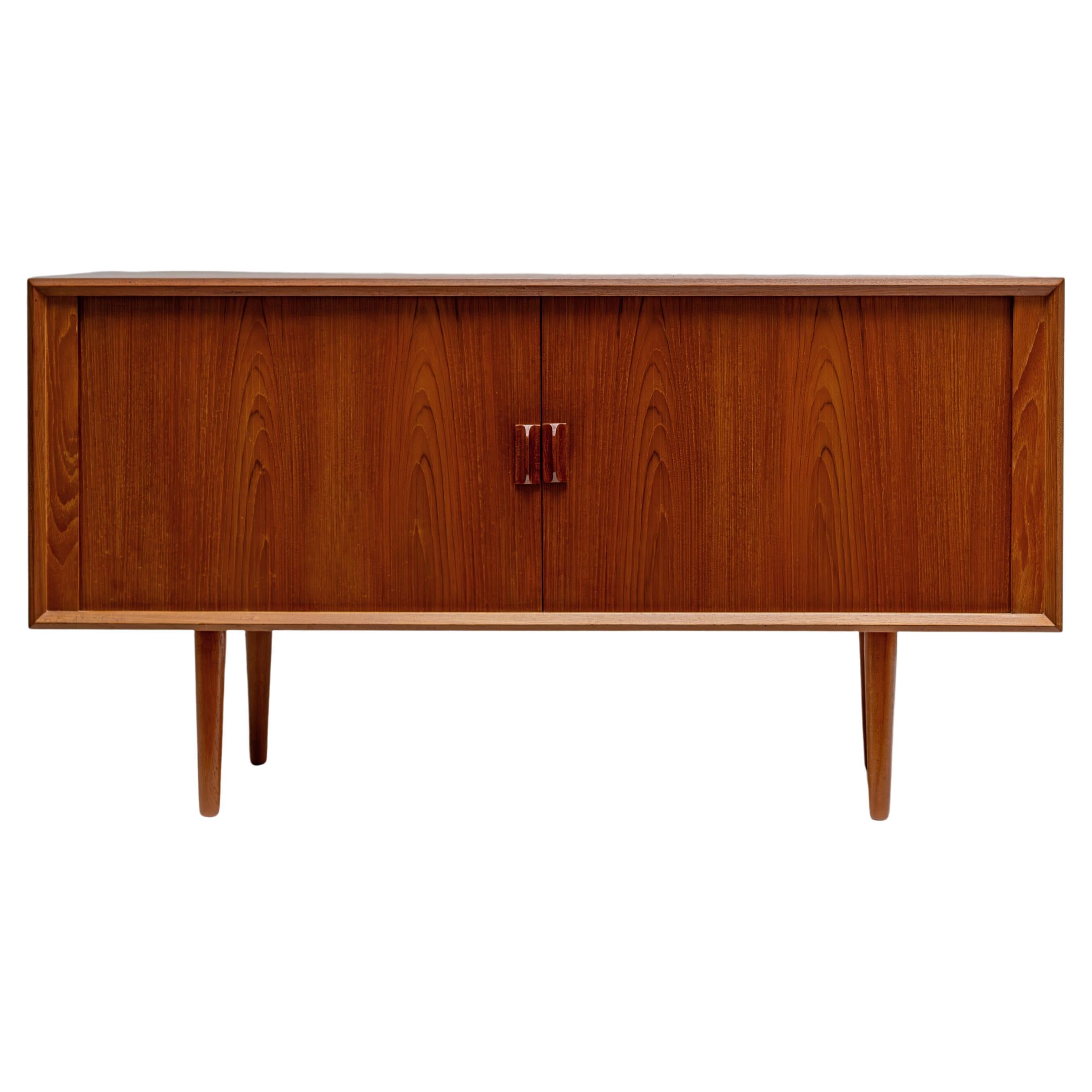 This mid-century teak credenza from the 1960s, designed by Svend Aage Larsen for Faarup Møbelfabrik, showcases premium Danish craftsmanship. The piece features elegant sliding tambour doors with finely sculpted pulls, opening to reveal interior