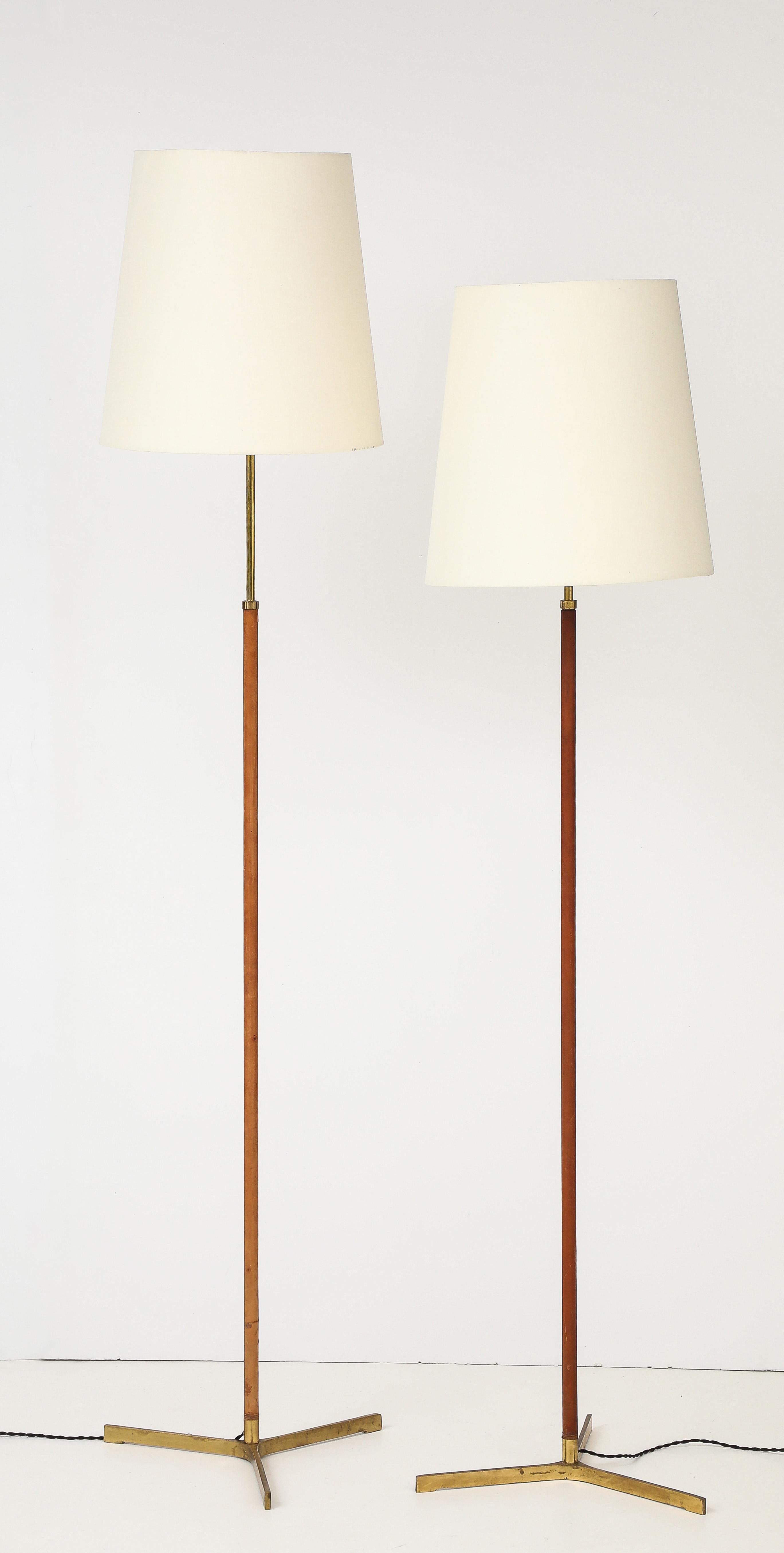 Rare pair of Svend Aage Holm-Sorenssen floor lamps, Denmark. 
Elegant and sophisticated pair of adjustable height floor lamps. Original leather wrapped and stitched center poles on sculpted brass tripod bases. Newer updated twisted fabric cord