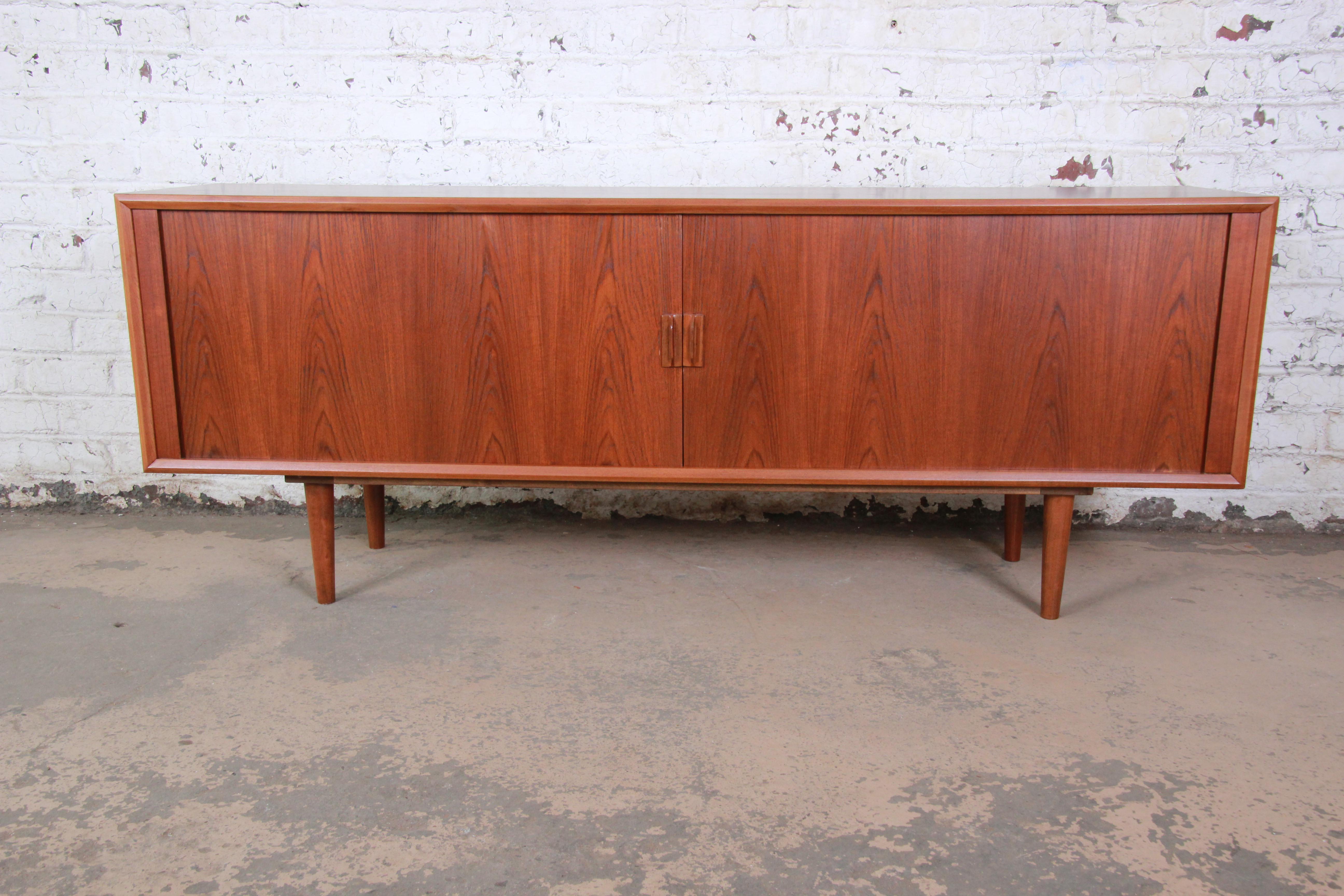 An exceptional midcentury Danish modern teak sideboard or credenza designed by Svend Aage Larsen for Faarup Møbelfabrik. The credenza features beautiful teak wood grain and sleek Danish design. It has a floating design, with four sculpted solid teak