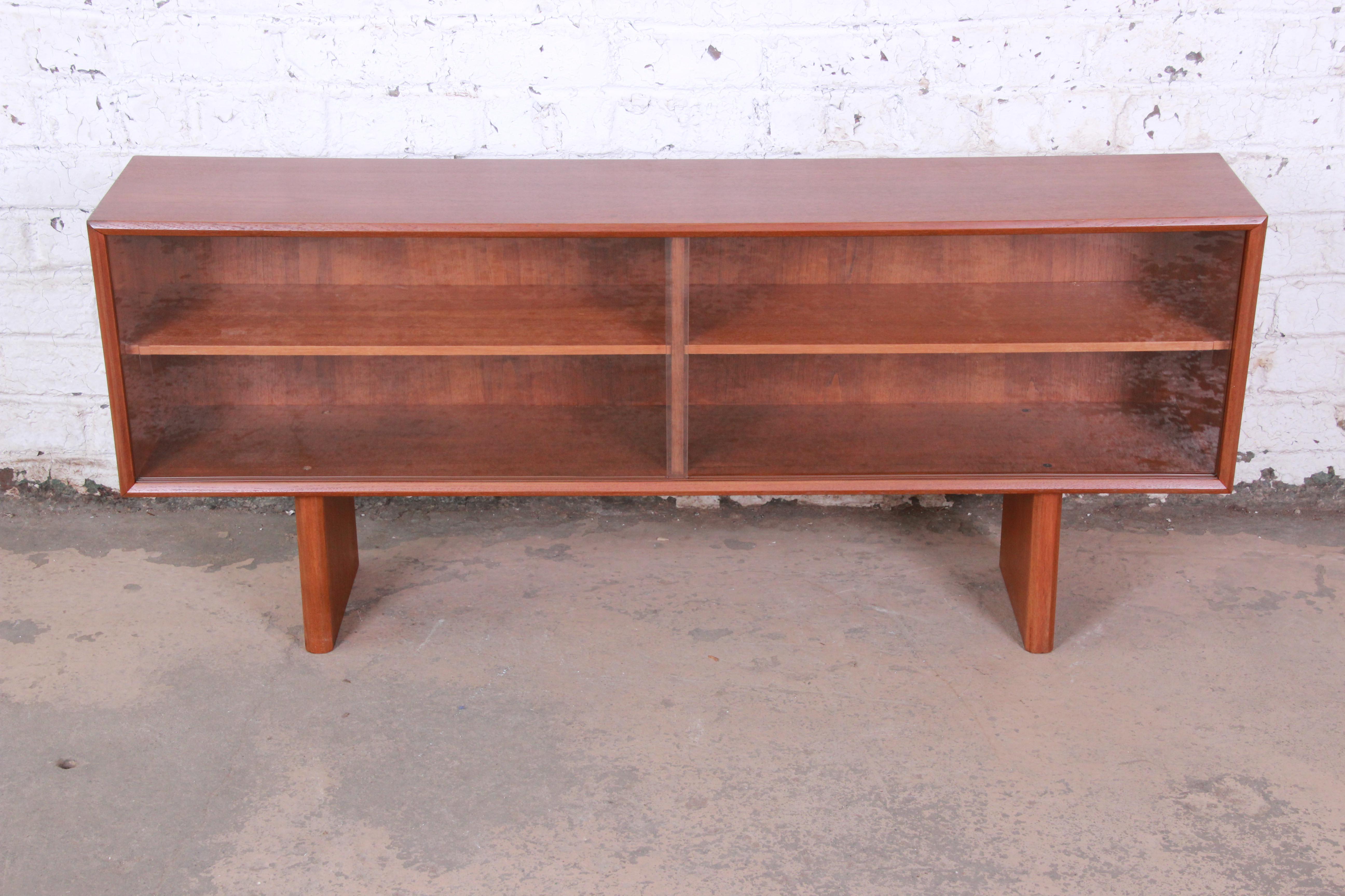 An exceptional midcentury Danish modern teak glass front bookcase or credenza designed by Svend Aage Larsen for Faarup Møbelfabrik. The credenza features beautiful teak wood grain and sleek Danish design. It has a floating design, with two sculpted