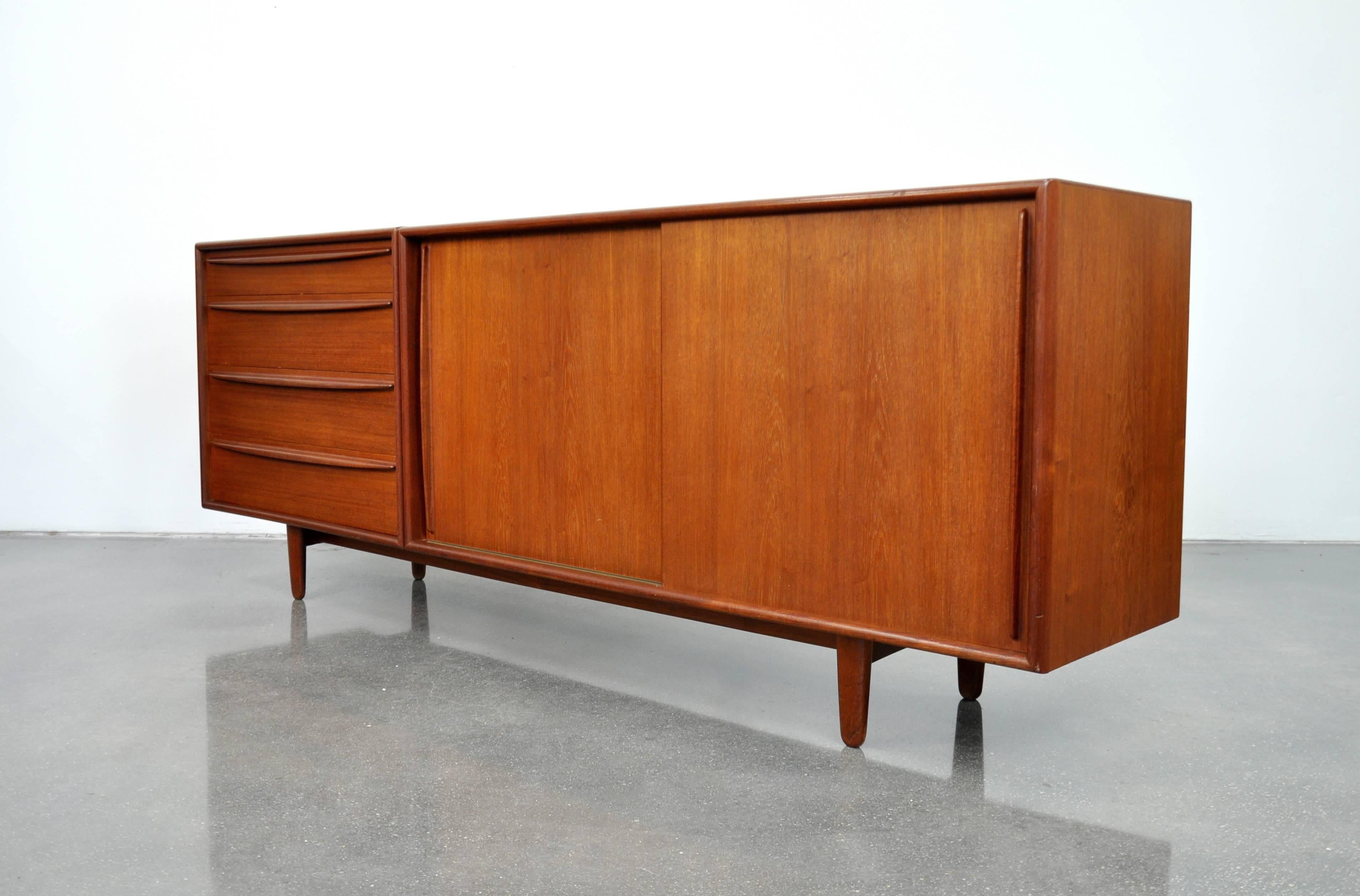 Beautiful midcentury Danish Modern teak bar cabinet, designed by Svend Madsen for Falster, made in Denmark in the 1960s. The sideboard features two sliding doors opening to an interior fitted with two (2) shelves and a felt-lined drawer, and a