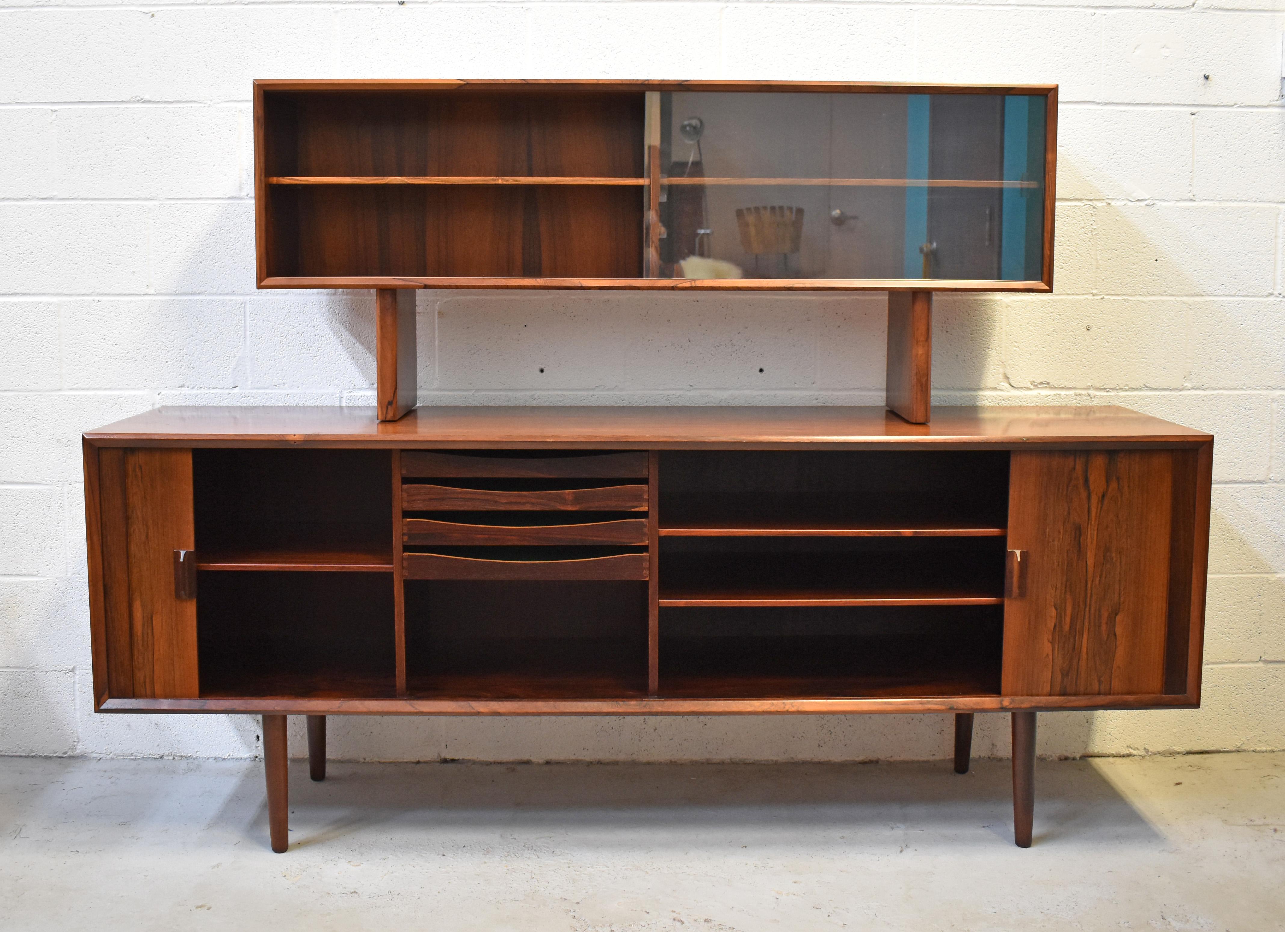 This stunning rosewood two-piece sideboard was designed by Svend Larsen for Faarup Møbelfabrik. The tamboured doors with book matched grain move smoothly and freely and open to reveal four green-felt lined drawers and shelving. The top unit is