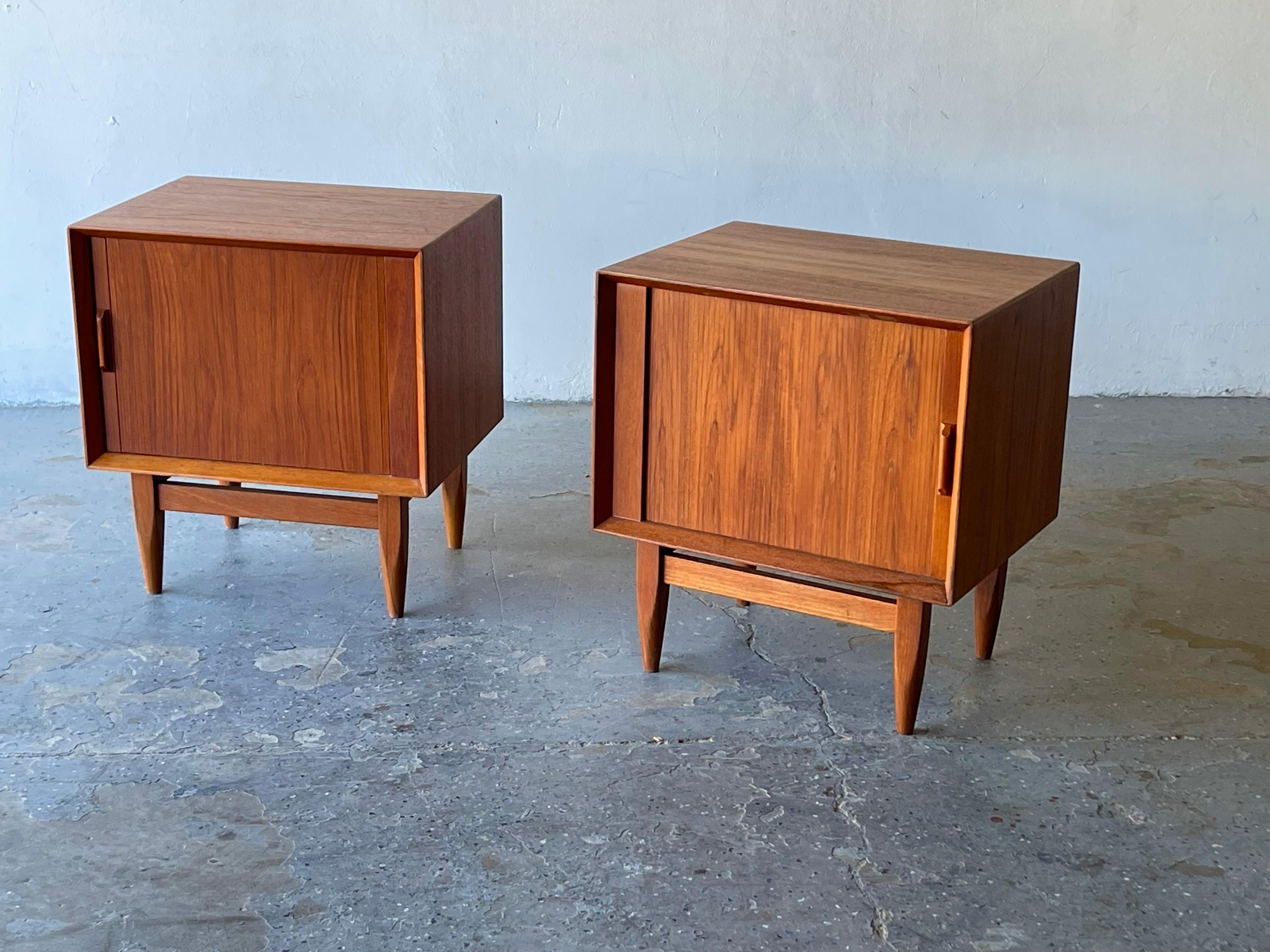 Pair of teak Scandinavian modern nightstands or end tables designed by Svend Madsen for Falster Denmark. Tambour doors slide smoothly to reveal an adjustable shelf and a pull out drawer. Cabinets are finished on all sides so that they may be floated