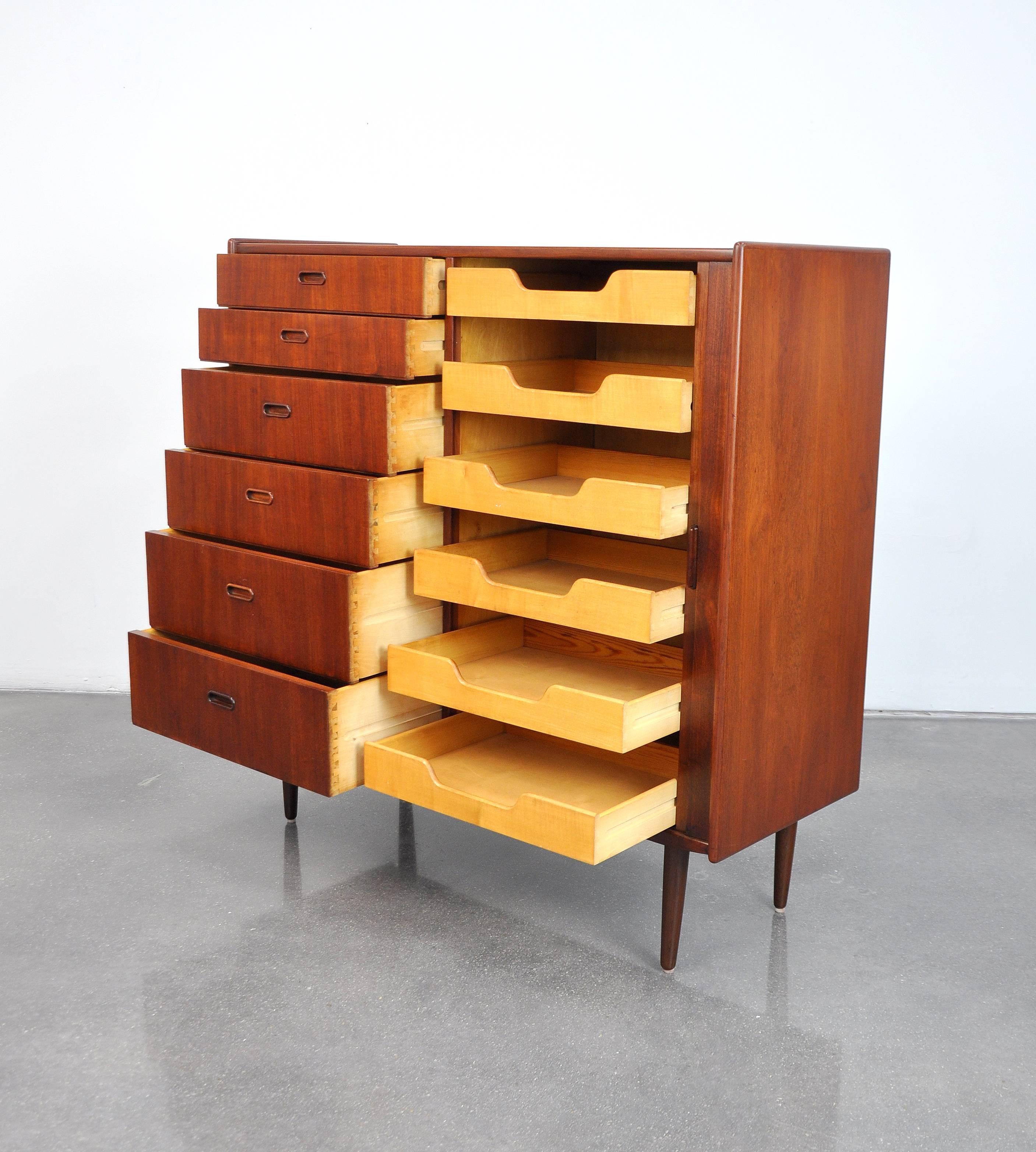 Both gorgeous and functional, this Mid-Century Danish Modern bachelor's chest of drawers dates from the 1960s. With a total of 12 drawers, it provides a ton of storage space. The vintage gentleman's wardrobe features sculpted teak handles, tambour