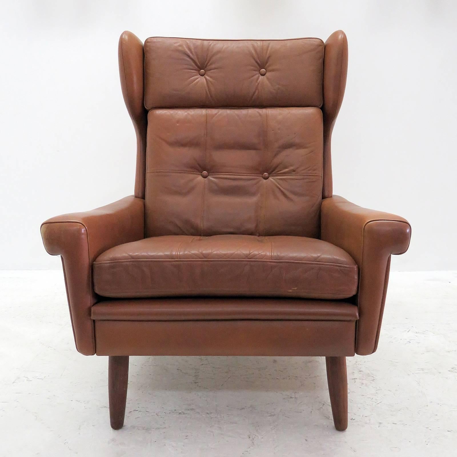 Wonderful high back winged leather lounge chair by Svend Skipper, with loose cushions upholstered in buttoned cognac colored leather with stained beech legs.