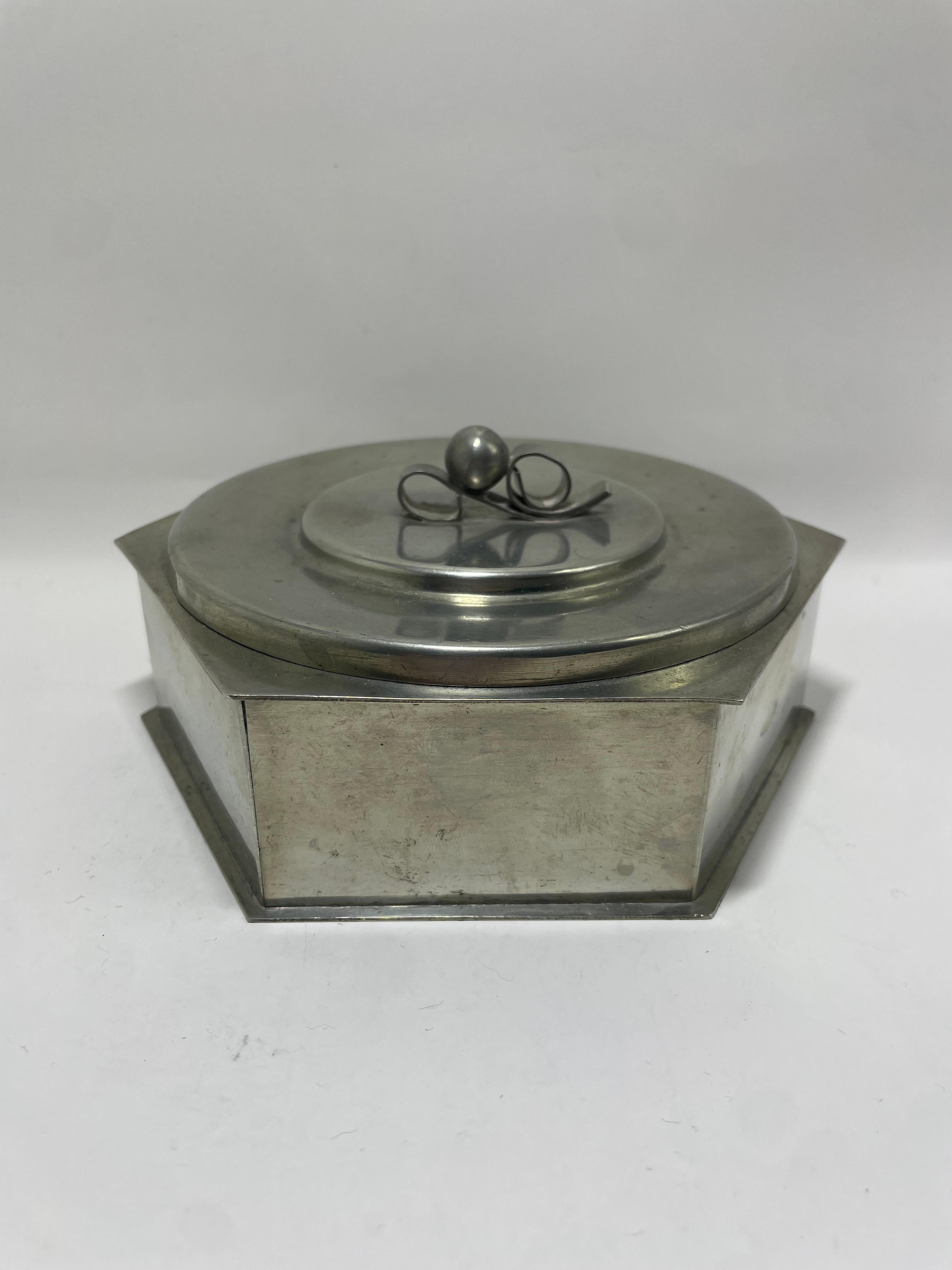 Rara y elegante caja hexagonal de peltre con tapa de Svenskt Tenn, fechada en 1936, que ejemplifica la refinada artesanía y el arte funcional del diseño sueco de principios del siglo XX. La caja presenta una limpia silueta geométrica con suaves