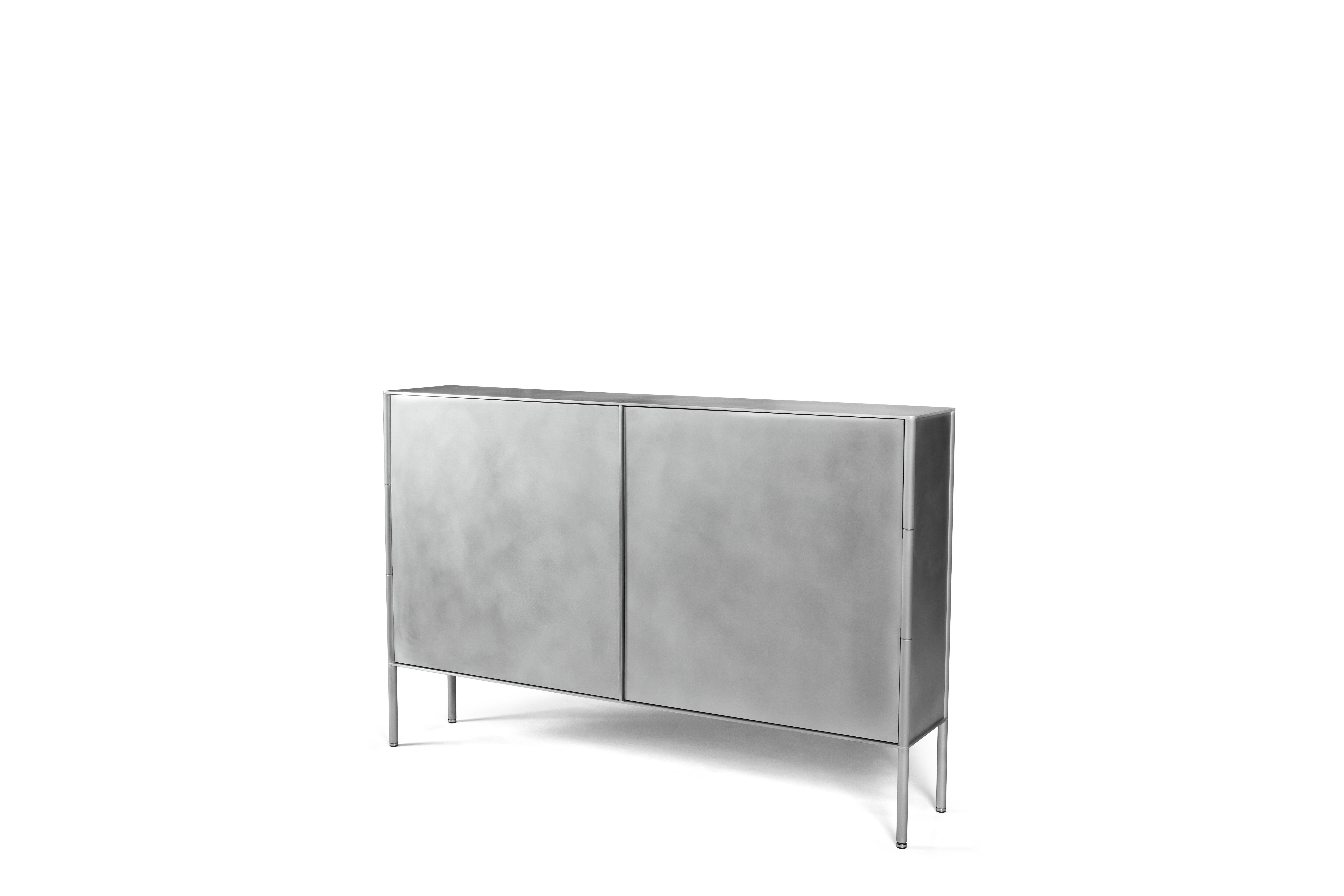 The SW cabinet by Jonathan Nesci is cut and machined aluminum with a waxed finish. The doors, back, and sides are milled into the legs. The doors are cut and are welded to machined custom hinges integrated into the legs. The doors open with a