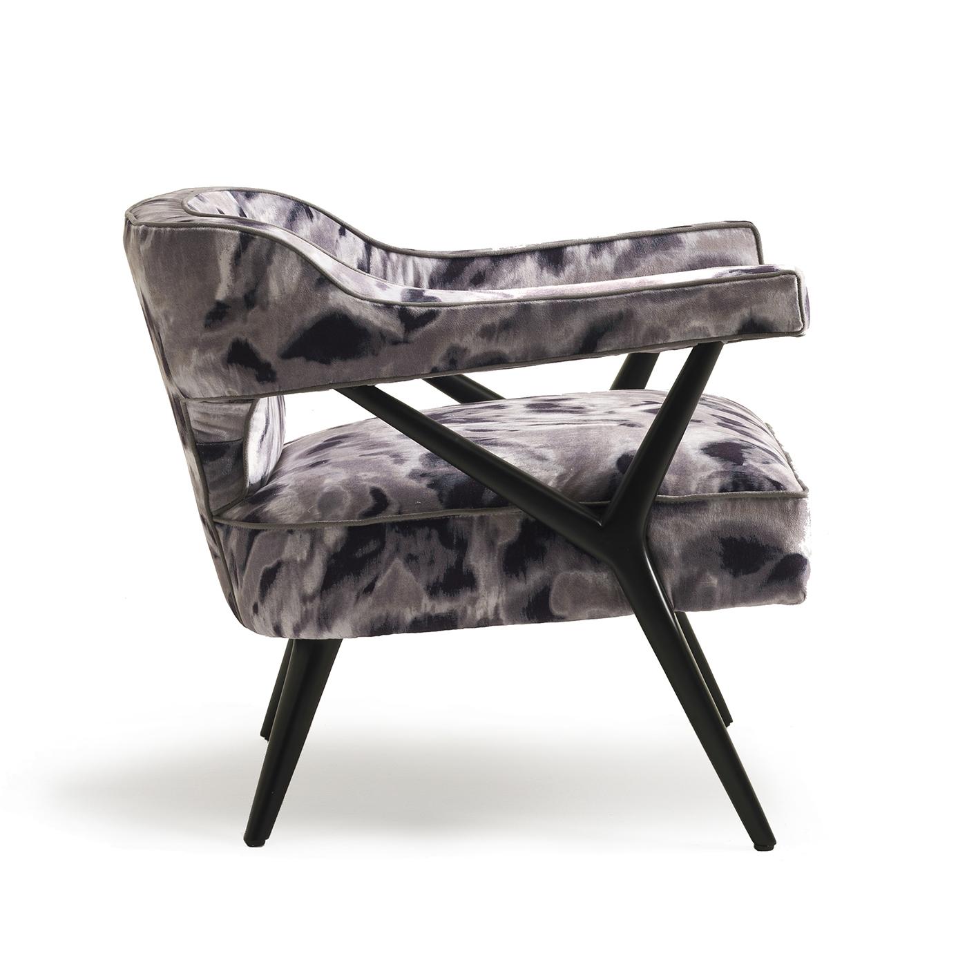 This lounge chair exudes elegant charm and timeless sophistication, thanks to the combination of a geometric structure in wood with a matte black finish supporting cut-out cushions upholstered in a stunning printed fabric in black, white, and grey.