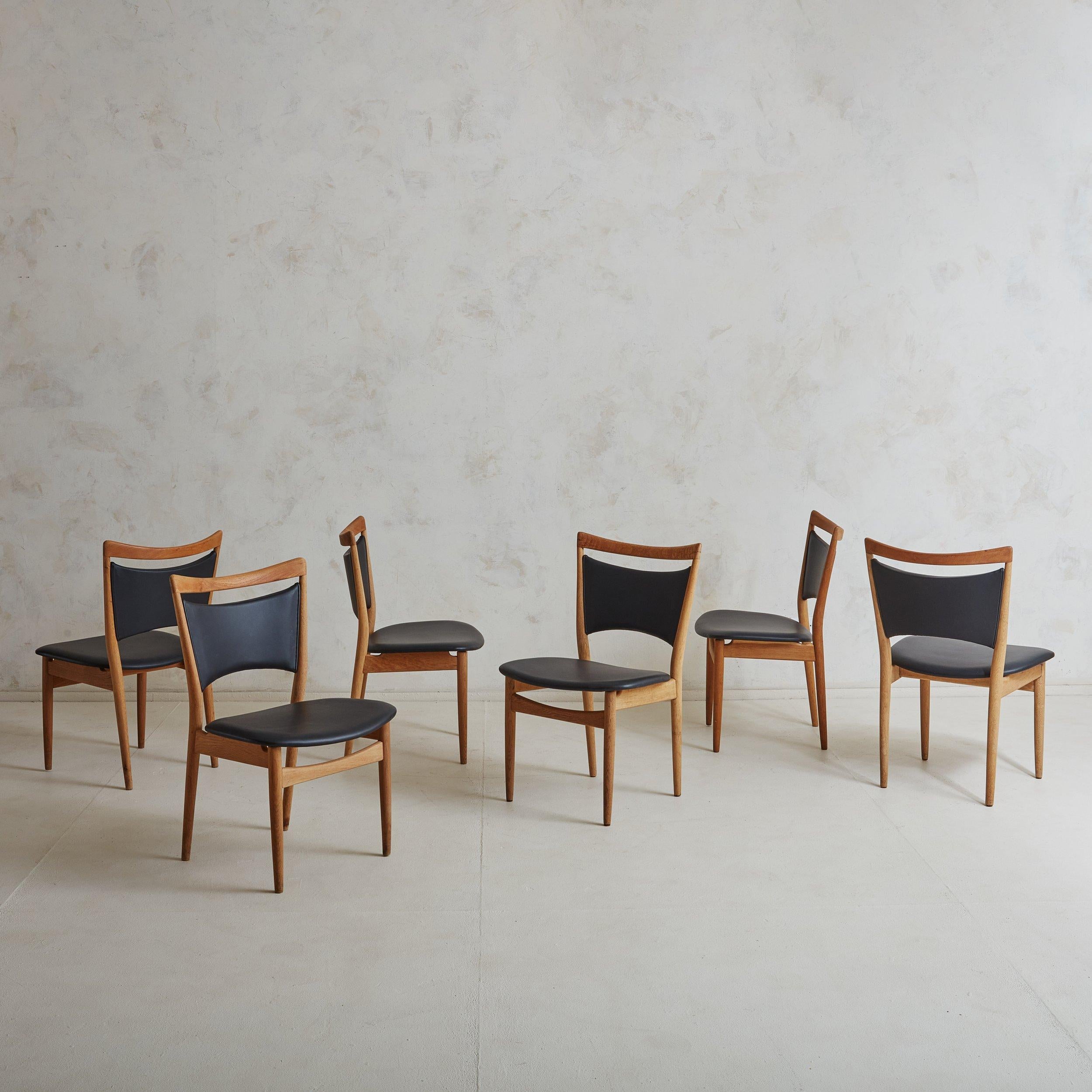 Sold and priced individually.

A 'SW86' black vinyl and oak dining chair by Danish furniture designer Finn Juhl for Søren Willadsen Møbelfabrik in the 1950s. This Scandinavian Modern sculptural dining chair features a warm honey hued oak frame with