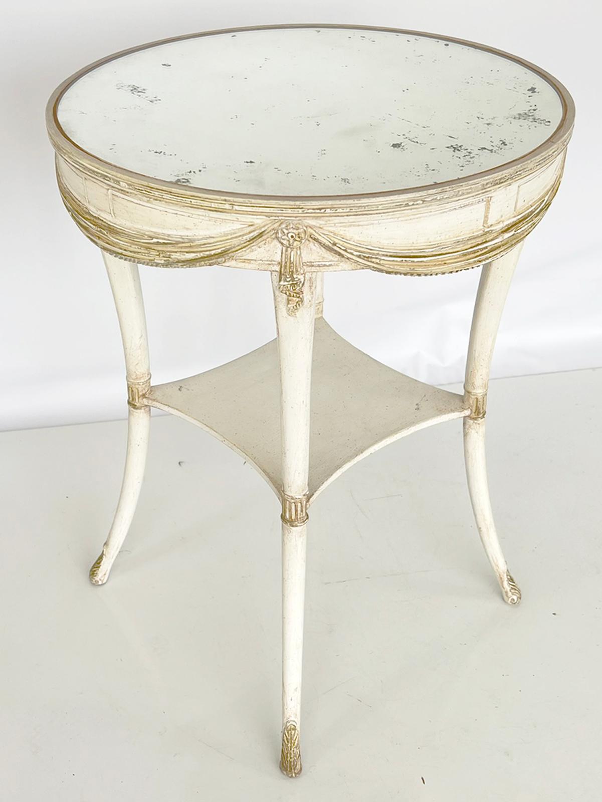 Round candlestand table, having an aged mirrored top, on painted table base, its apron decorated with carved swags centered between draped rosettes. The table is raised on four, round, tapering, splayed legs, joined by a shelf stretcher with concave
