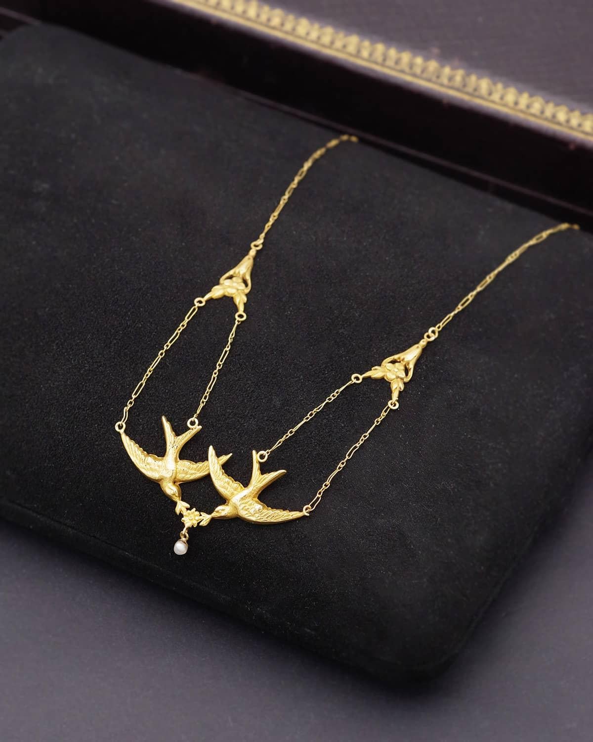 Collar de golondrina Art Nouveau en oro de 18 quilates. Collar drapeado adornado con un par de golondrinas que sostienen una pequeña flor y una perla fina. Las golondrinas están sujetas por dos cadenas y un elemento adornado con pequeñas flores.