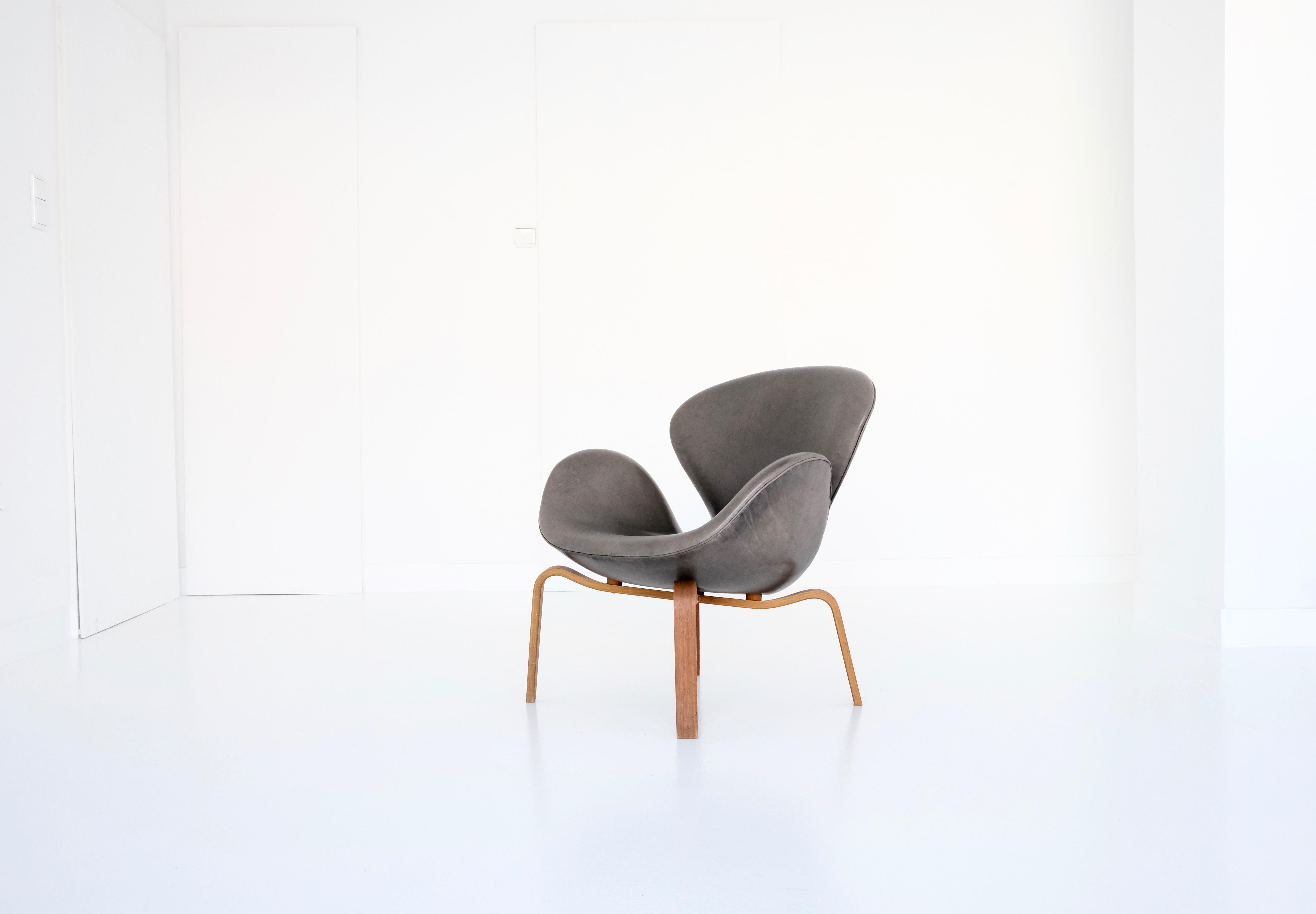 An extremely rare vintage Swan chair with a wooden frame and black leather upholstery, bleached by sunlight to a beautiful, deep and warm dark gray. While the ’swan series‘ is still in production today by Fritz Hansen, Denmark, the „wooden version“