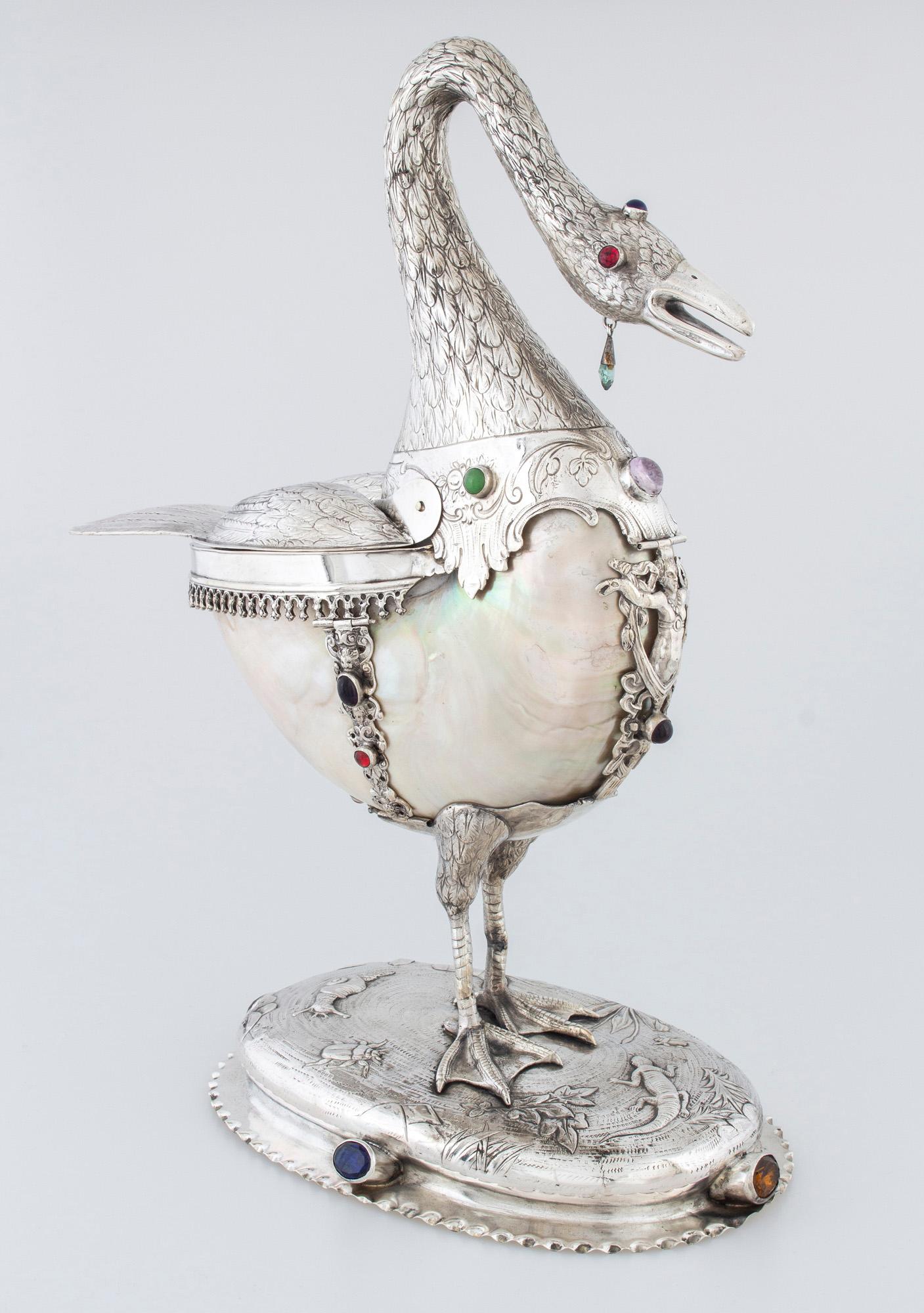Silver centerpiece. Gross weight: 1135 g. 
Swan-shaped silver-encased shell (nautilus). 
With a wavy rim, an oval base depicting a naturalistically crafted waterside scene. 
On it, there are embossed and engraved decorations. 
On the sides of the