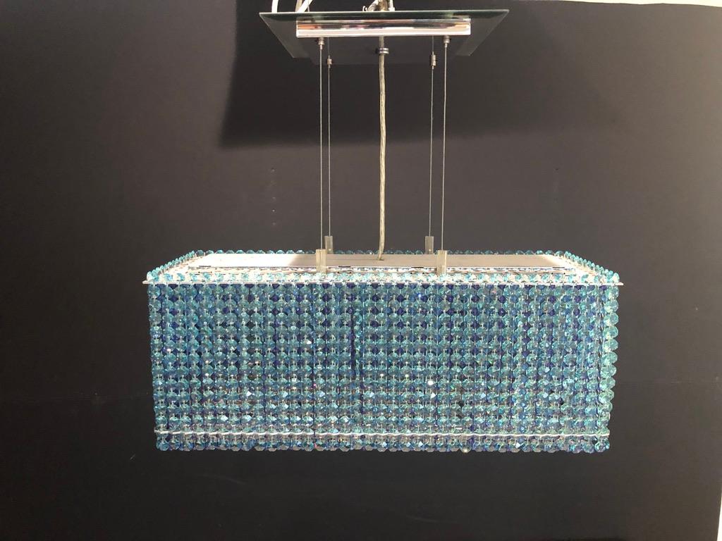 Brillant cristal Swarovski, clair, aqua, bleu et violet coloré en forme de boîte, lustre de suspension moderne à 6 lumières. Plaque de plafond en chrome poli et miroir, avec supports de câbles avec cordon électrique central.
Mesure : Hauteur de