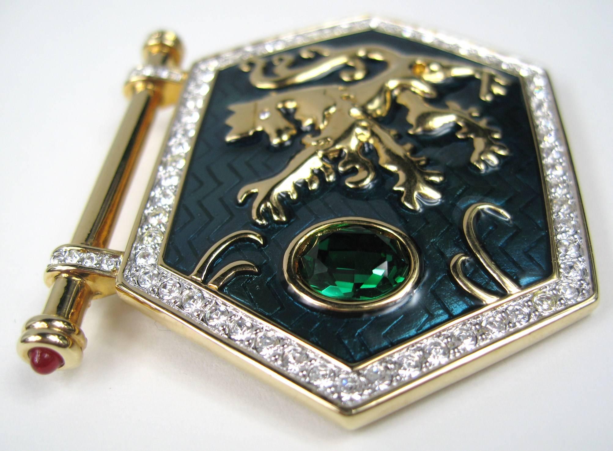 Swarovski Brooch Gold Griffin set over green enamel with a large green Swarovski Crystal then surrounded by clear crystals. It has a bar across with red cabochons set on both ends Measures 2.38 in o 60.64mm wide x 2.06 in or 52.54mm top to bottom.