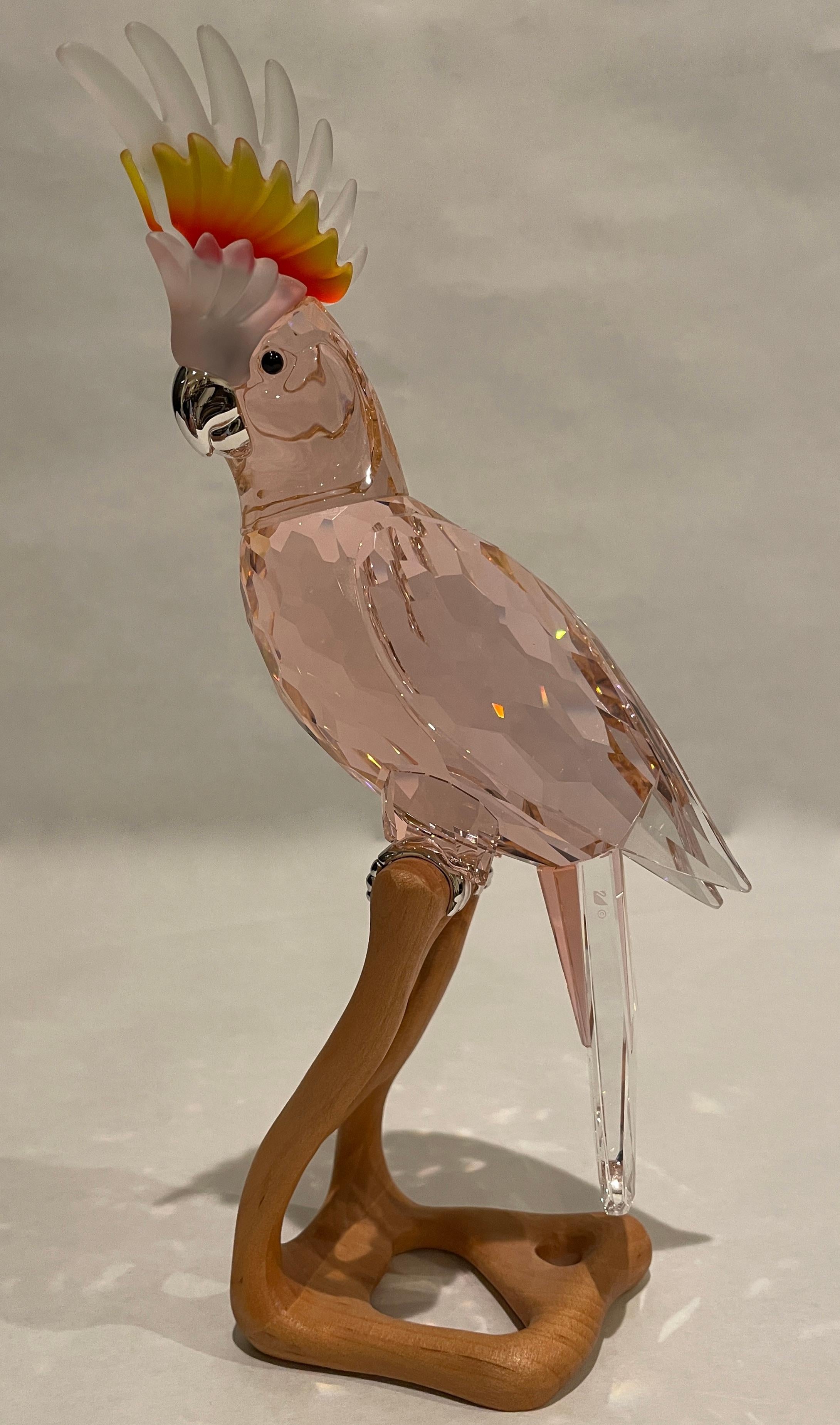 This retired Swarovski crystal Paradise bird is the Cockatoo. Made from kakadu red crystal (which is more of a dark pink colour) and sits on a wooden base.

Roland Schuster was commissioned to created a limited edition of crystal birds on wooden