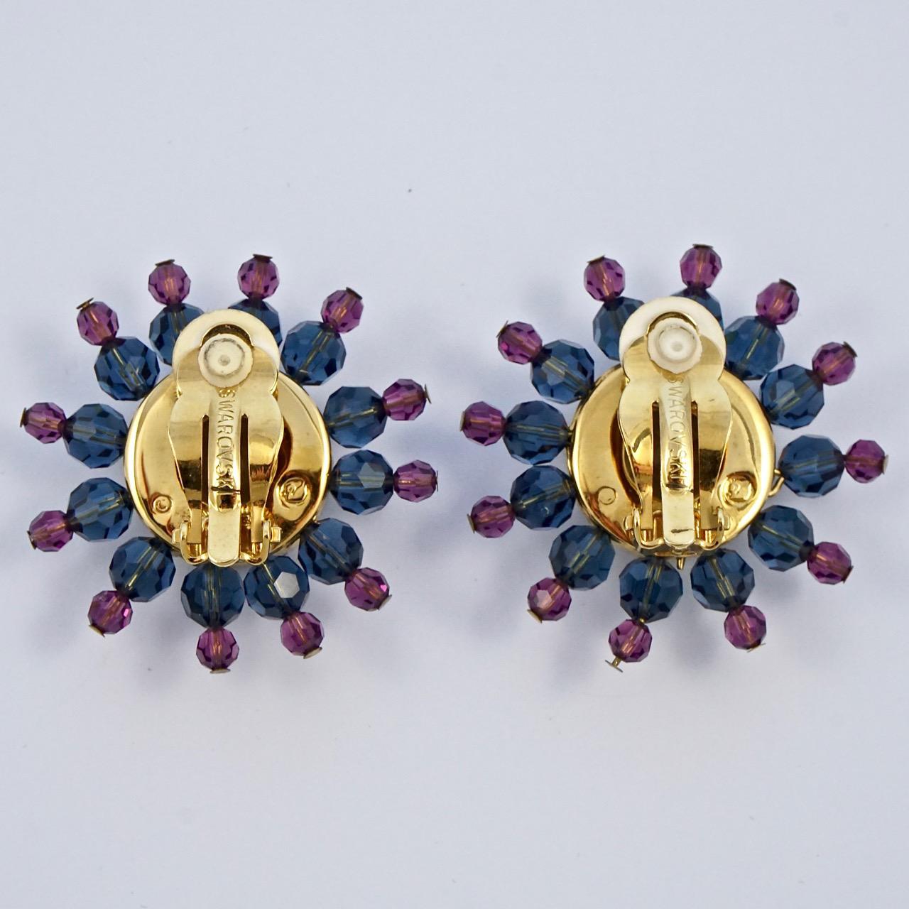 Preciosos pendientes de clip Swarovski chapados en oro con un precioso centro dorado y rodeados de cristales azules y rosas. Los pendientes llevan estampado el logotipo del cisne de Swarovski. Mide 3,8 cm de diámetro. Los pendientes están en muy