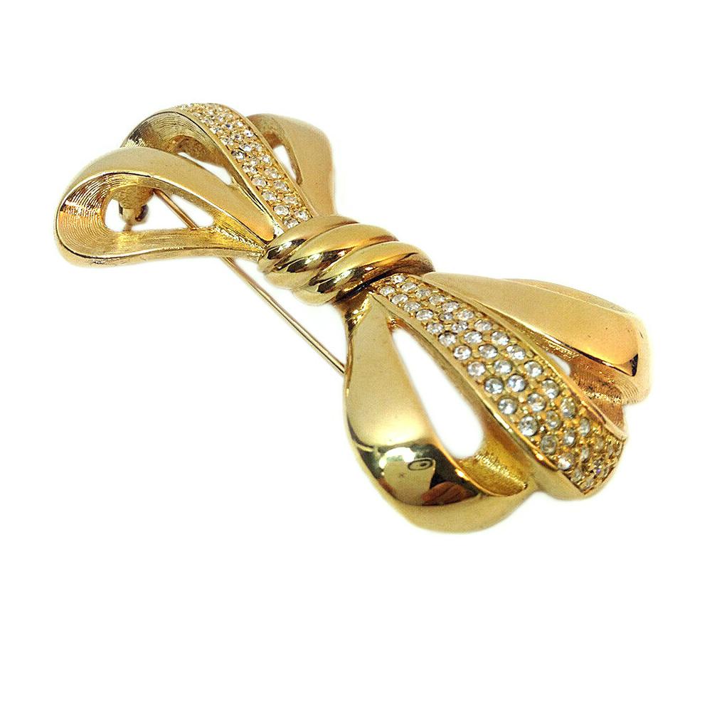 This is a stylish Swarovski gold-tone metal bow brooch with pavé-set clear crystals laid out on one band. Marked S.A.L. (Swarovski American, Ltd.) on the back of brooch. This mark was used from 1977-1989. It is an early version of Swarovski North