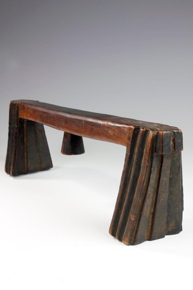 The form of this Swazi headrest consists of an upper section supported by two tapering legs, fluted with vertical grooves. 

A central lug features on the underside of the headrest, next to an old label. This label provides an insight into the story