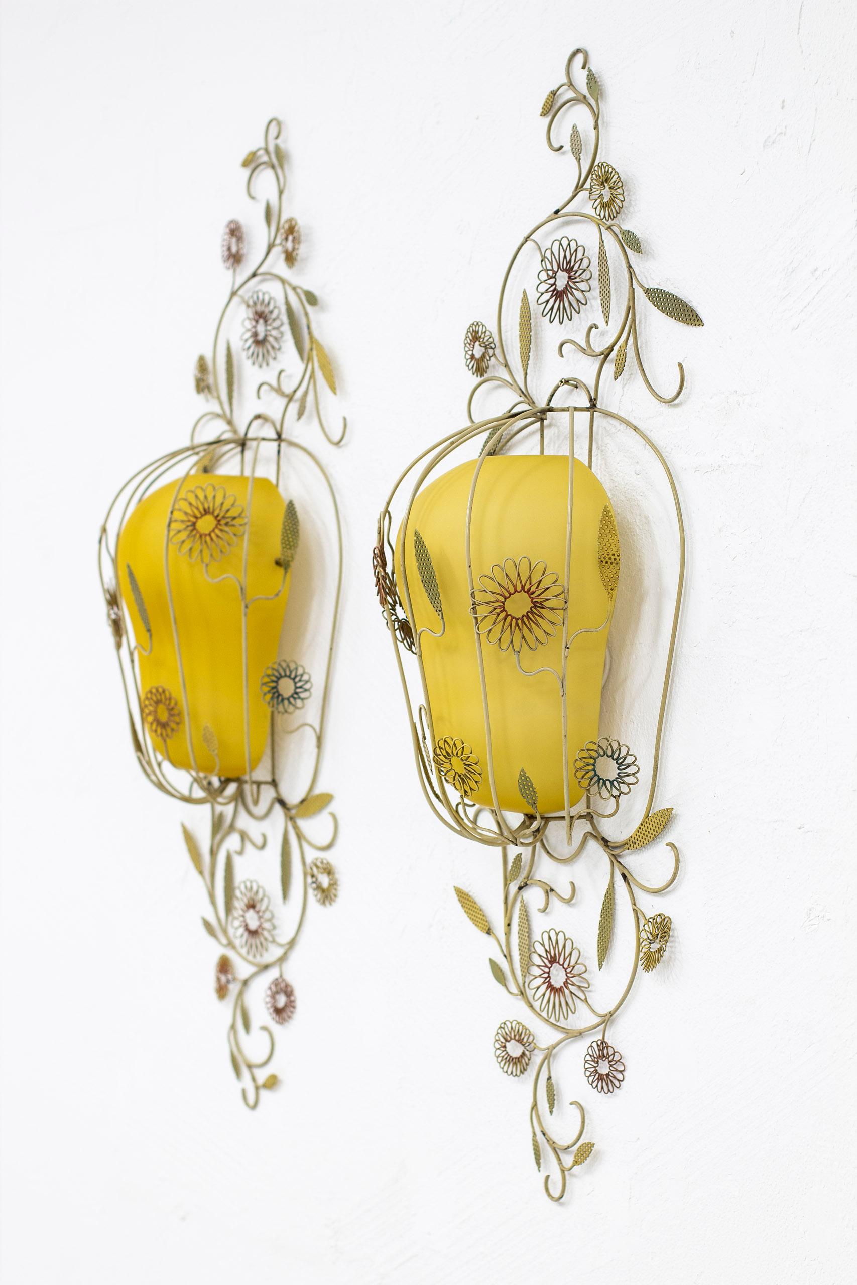 Rare wall lamps produced in Stockholm, Sweden by Corona Belysning. Made sometime between the 1940-1950s. Polychromed lacquered metal frame with stylized leaves and flowers. Opal glass shades in white and yellow glass. Very good vintage condition