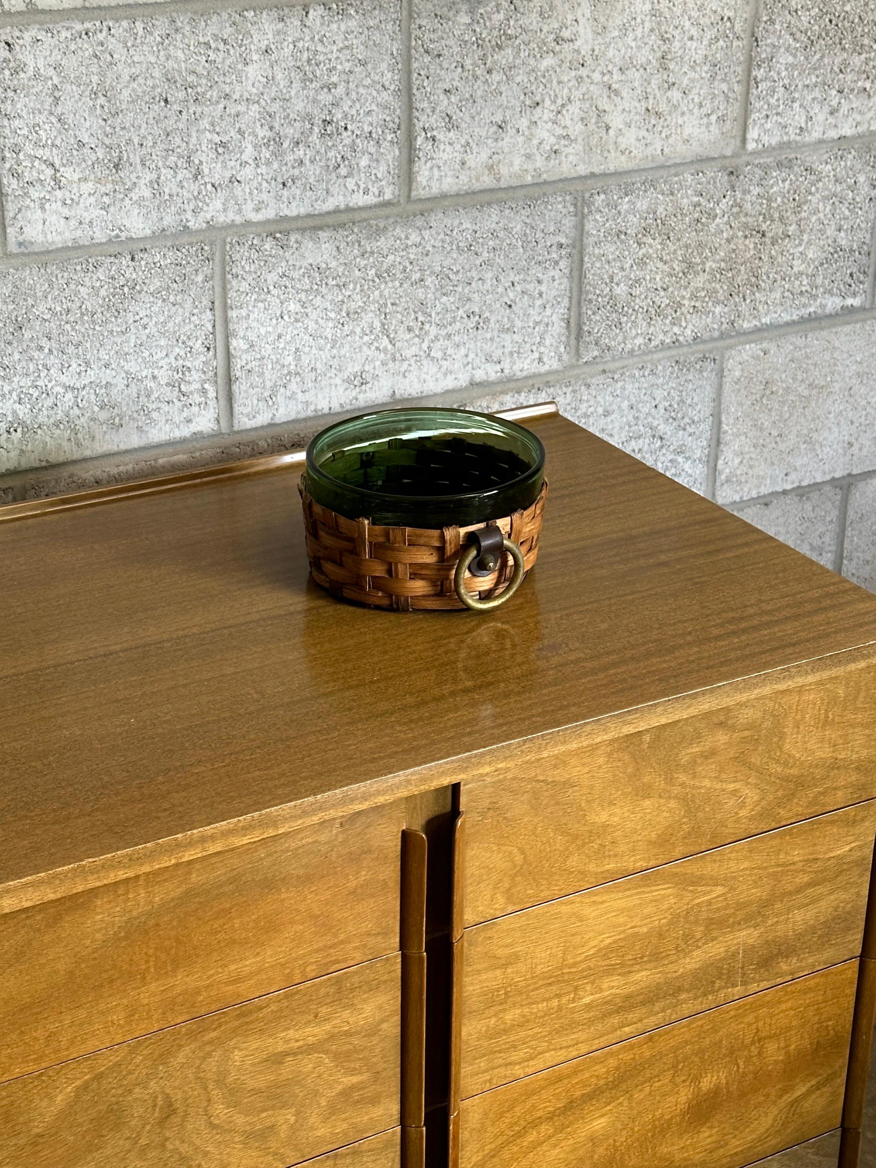 Un'attraente ciotola realizzata in vetro verde e circondata da una ciotola in vimini con maniglie in finto ottone. Un design scandinavo davvero eccezionale con una bella miscela di materiali e colori. Can si adatta a una varietà di interni e decori. 