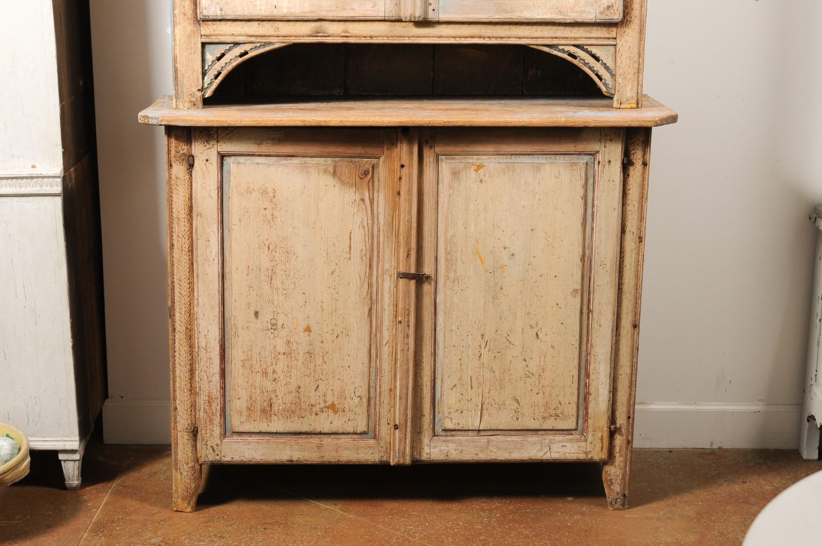 A Swedish early Gustavian period two-part wooden cabinet from the late 18th century, with original paint, carved accents, dentil molding, four doors and distressed patina. Created in Sweden during the last quarter of the 18th century, this wooden